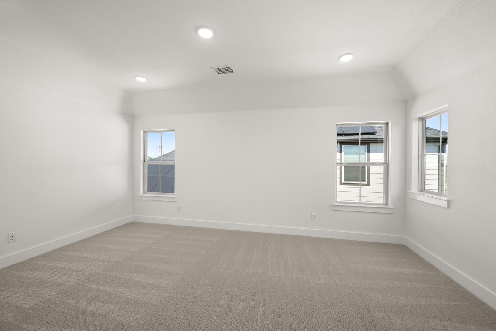 An empty, well-lit room with white walls, hardwood floors, and several windows providing natural light.