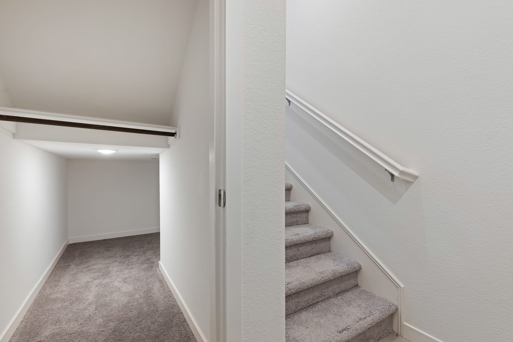 A narrow hallway with a staircase leading up, the walls and floor are painted in neutral tones, creating a minimalist and clean aesthetic.