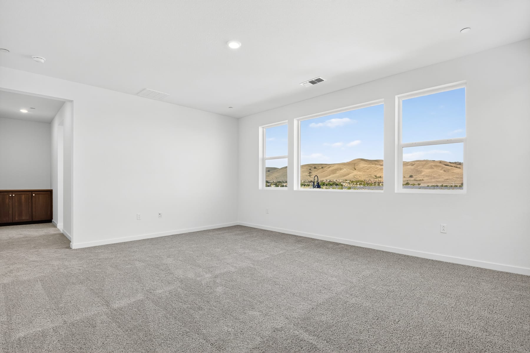 A spacious, well-lit room with large windows overlooking a scenic landscape of rolling hills and a clear sky.