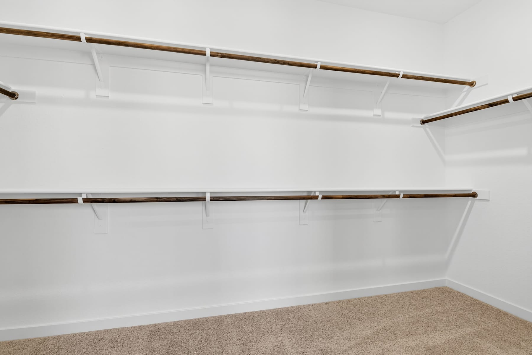 A white, empty closet with wooden shelves and a carpeted floor.