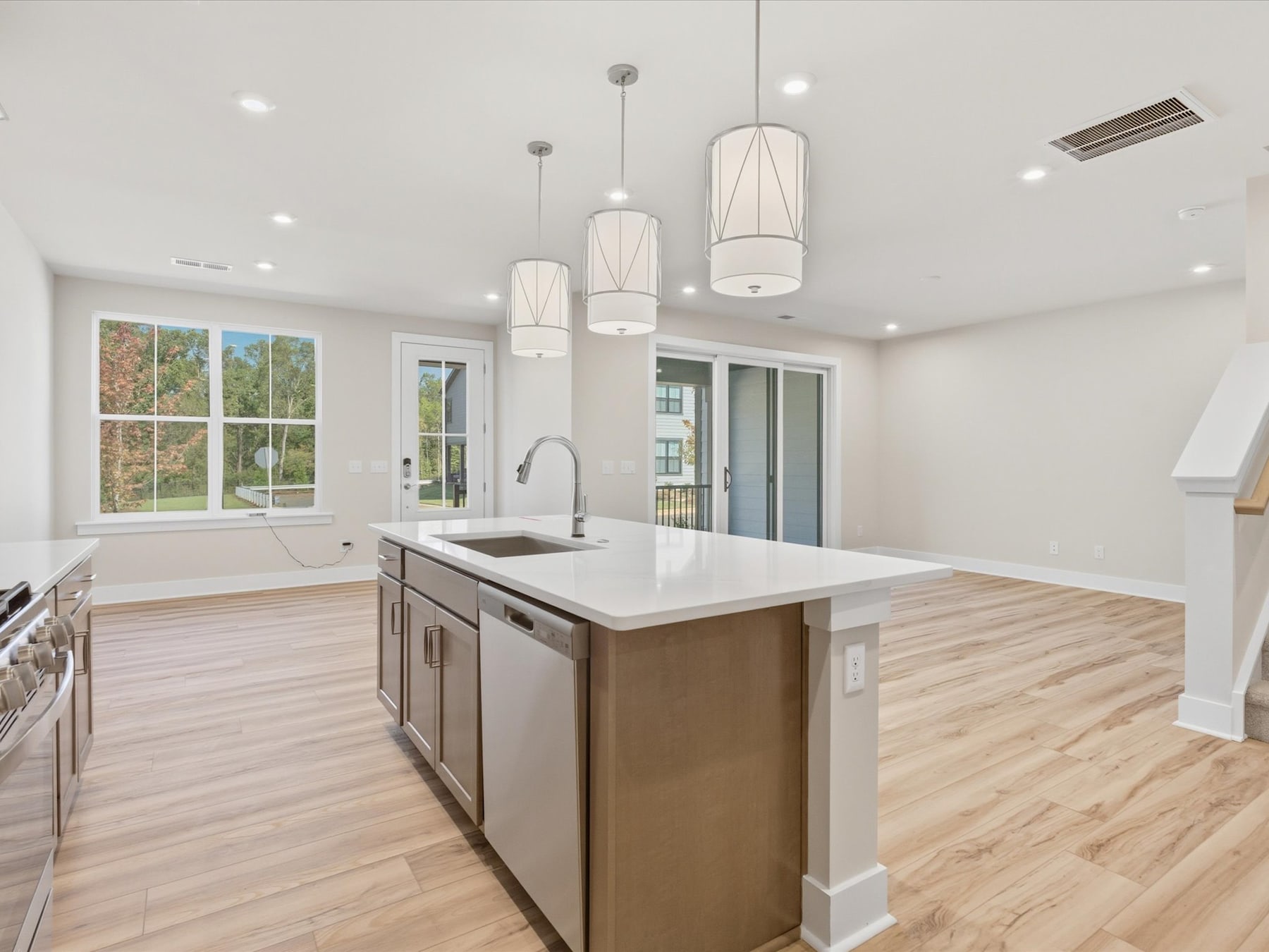 A modern, open-concept kitchen with a large island, pendant lighting, and hardwood floors, surrounded by large windows overlooking a scenic outdoor view.