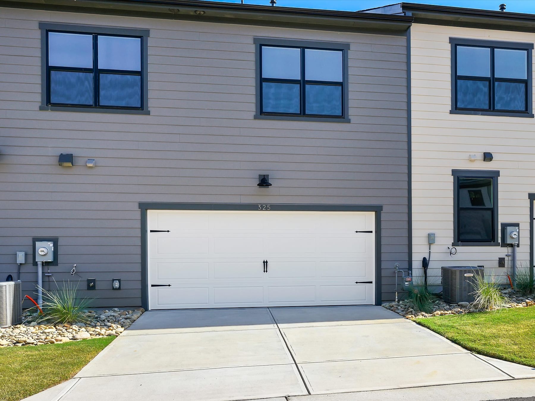 A modern, two-story residential building with a white exterior, a large garage door, and a well-maintained lawn in the foreground.
