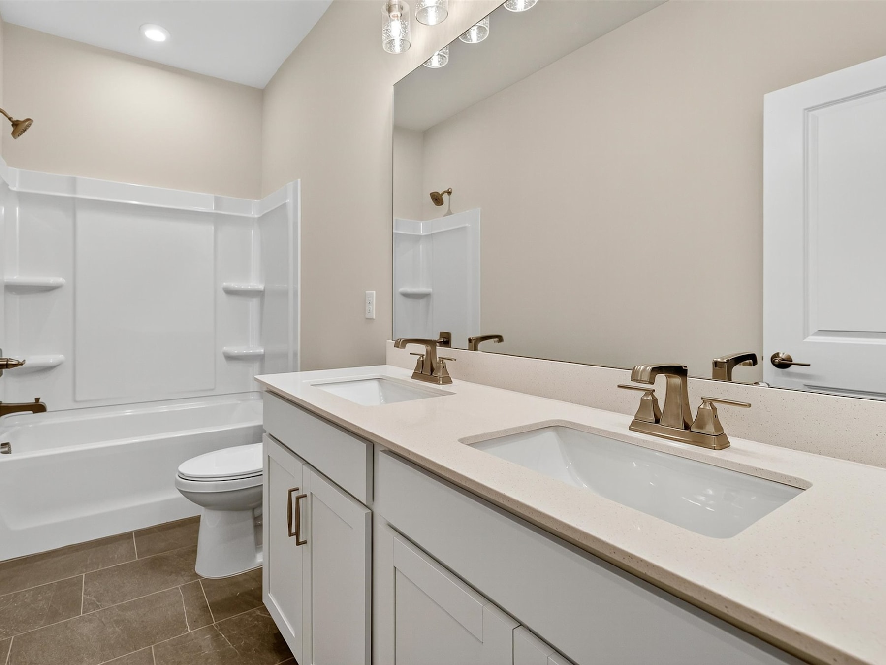 A modern and well-designed bathroom with a white vanity, double sinks, and a tiled floor. The walls are painted in a neutral color, and the room is illuminated by a stylish light fixture.