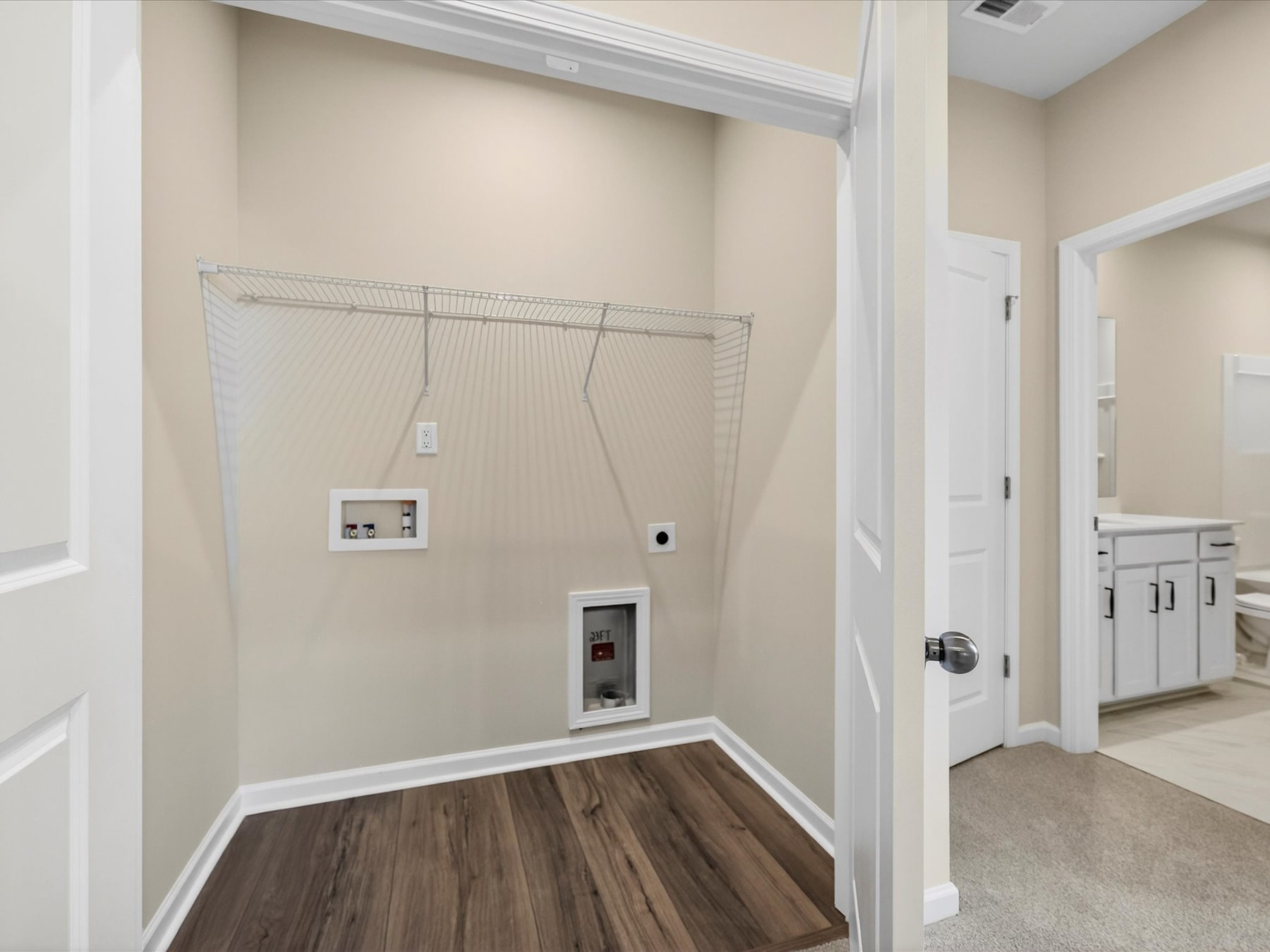 A spacious room with a wooden floor, a hanging clothes rack, and a white door leading to another room.