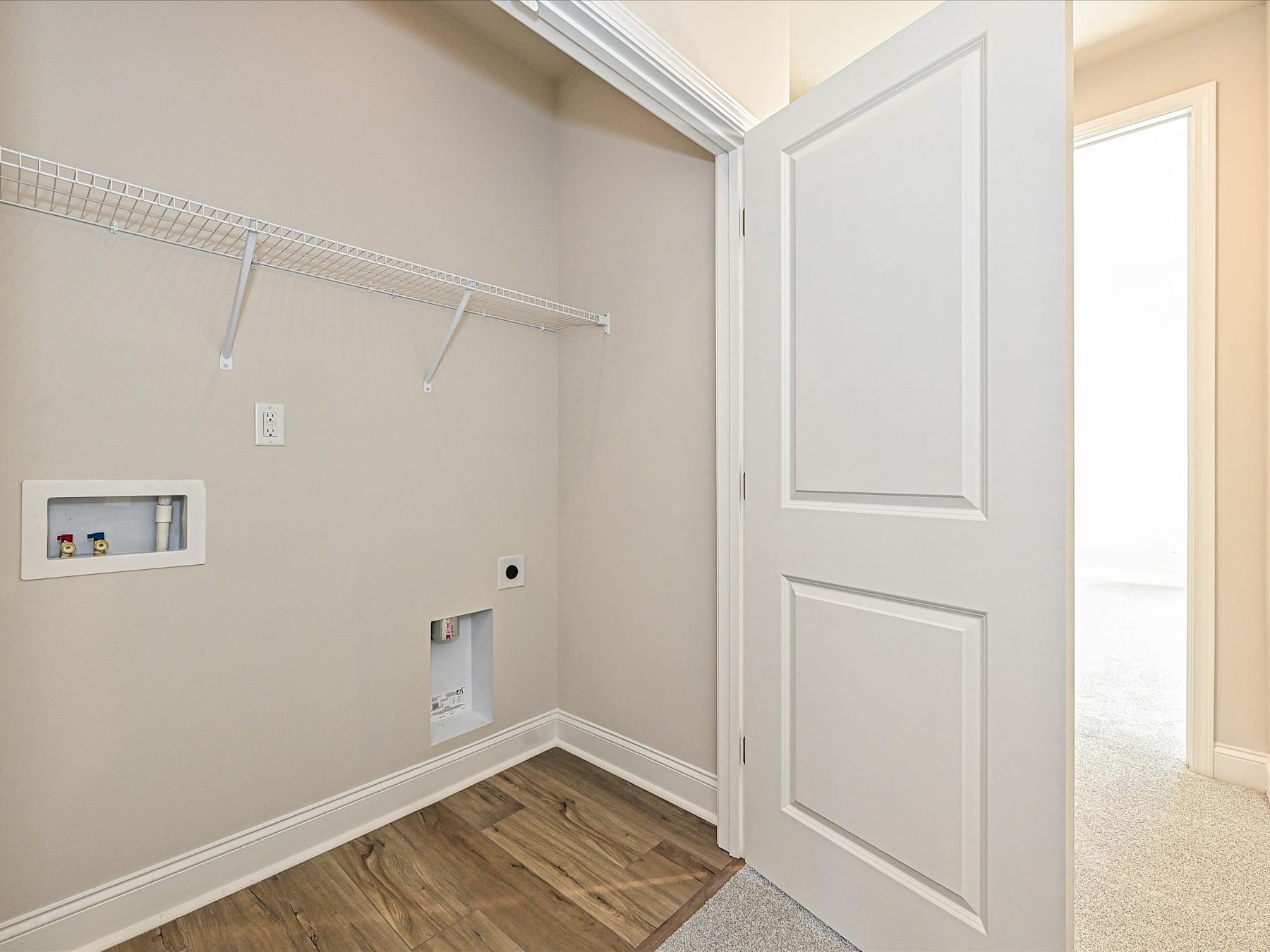 A small, well-lit room with a white door, a closet rod, and a wooden floor.