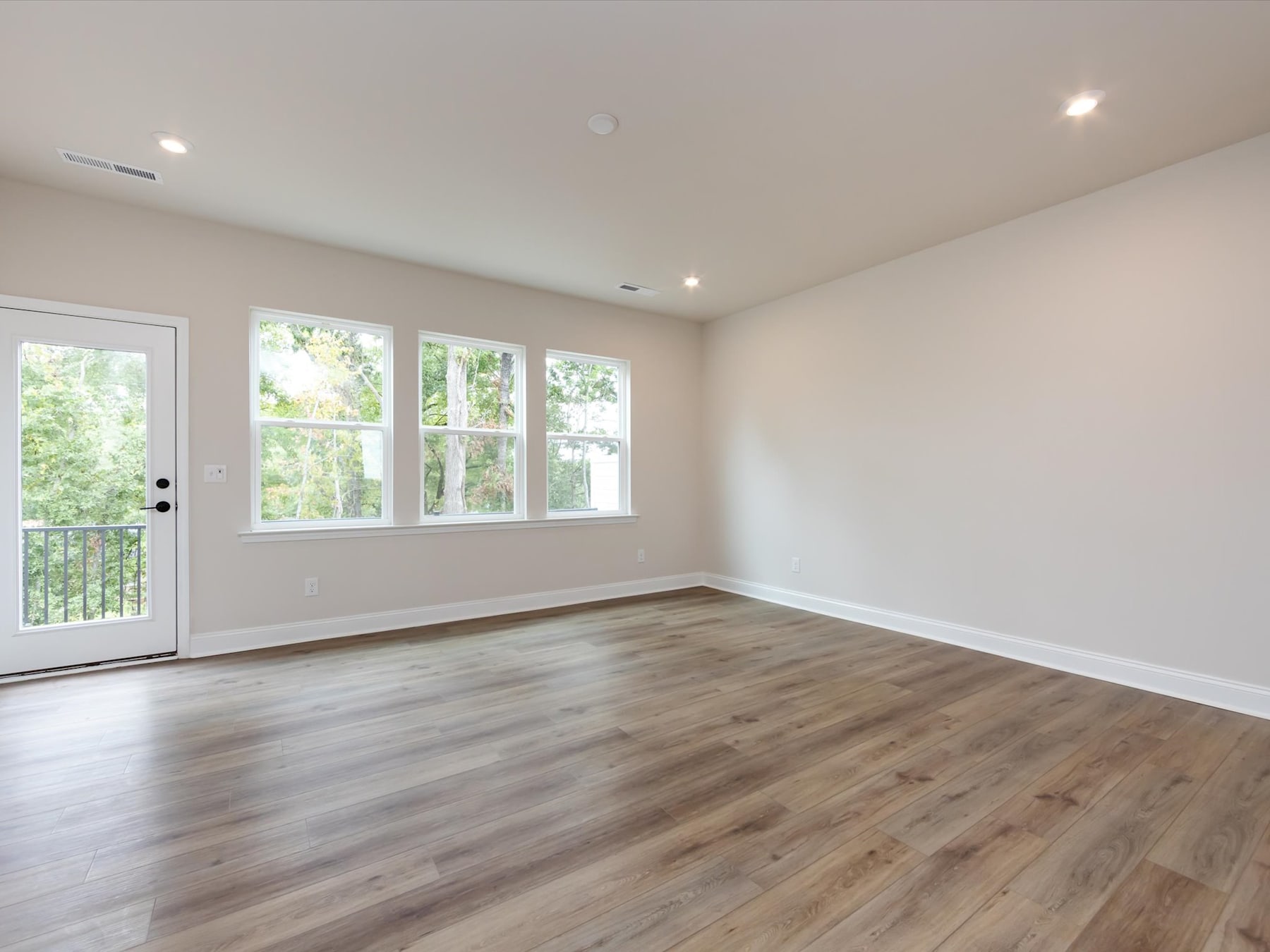 A bright and spacious room with large windows overlooking a lush, green outdoor area, featuring hardwood floors and a neutral color scheme.