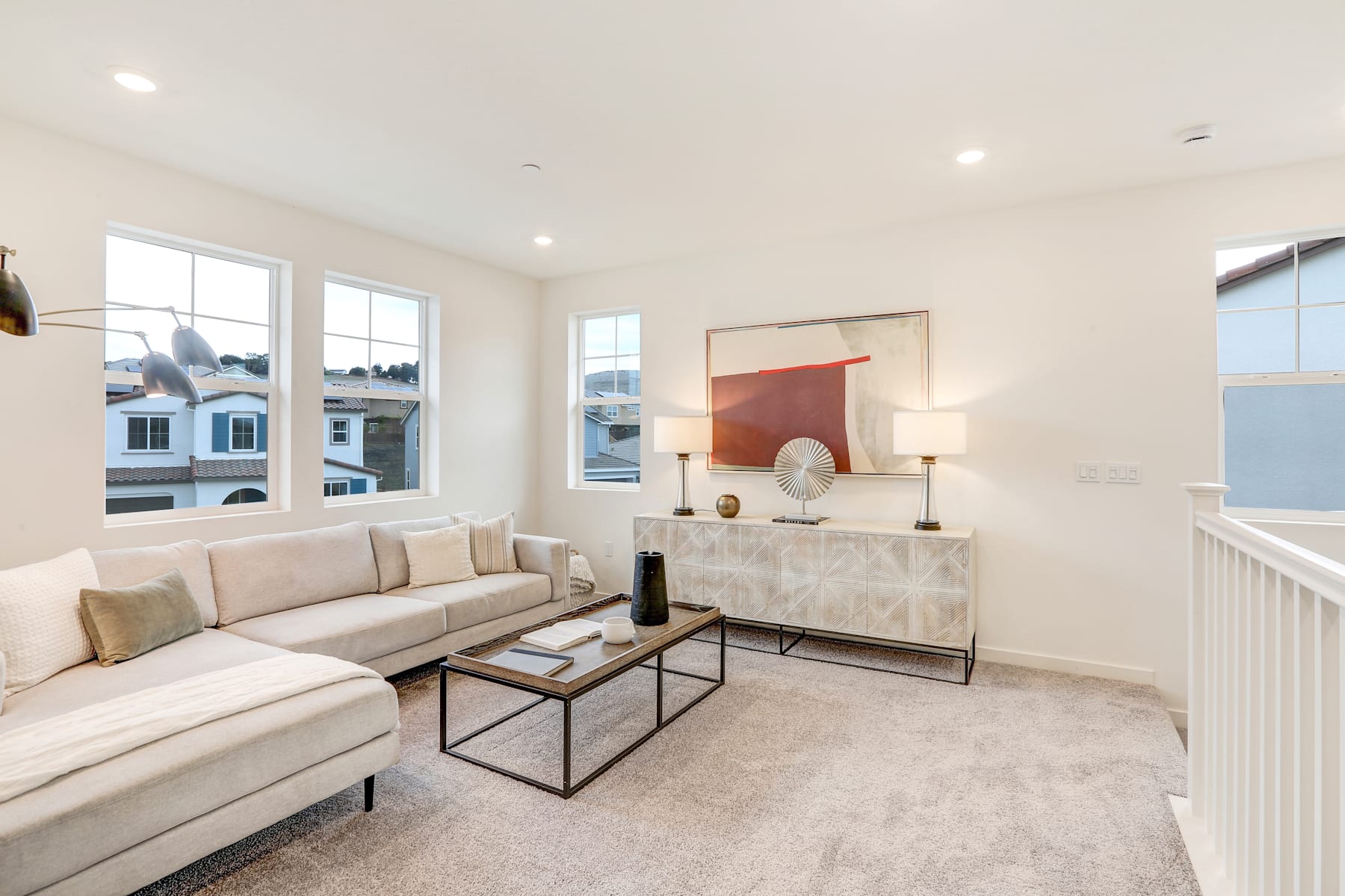 A cozy and modern living room with a beige sofa, a wooden console table, and a large window overlooking the cityscape in the background.