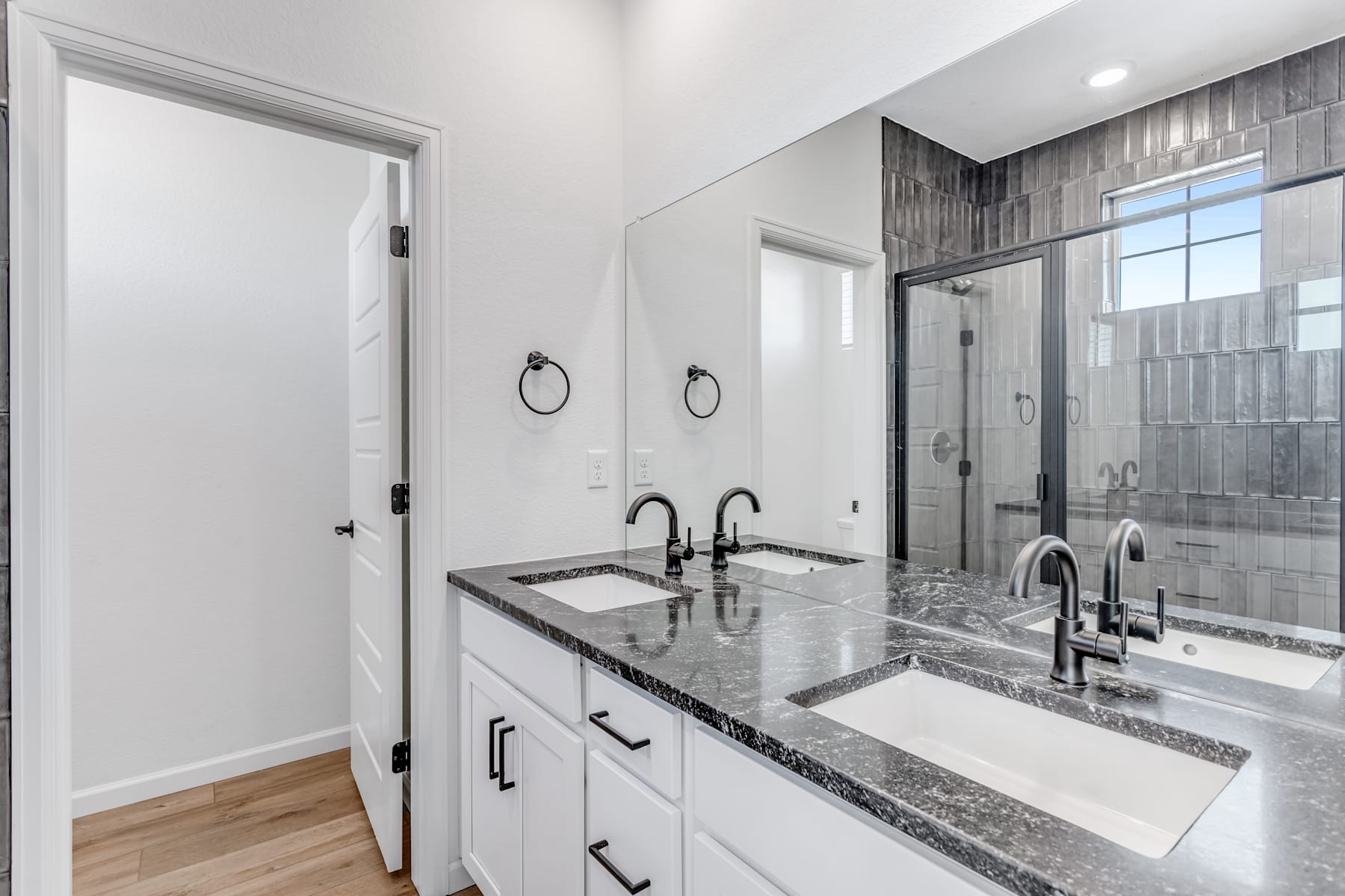 A modern and sleek bathroom with white cabinets, granite countertops, and a glass-enclosed shower area.