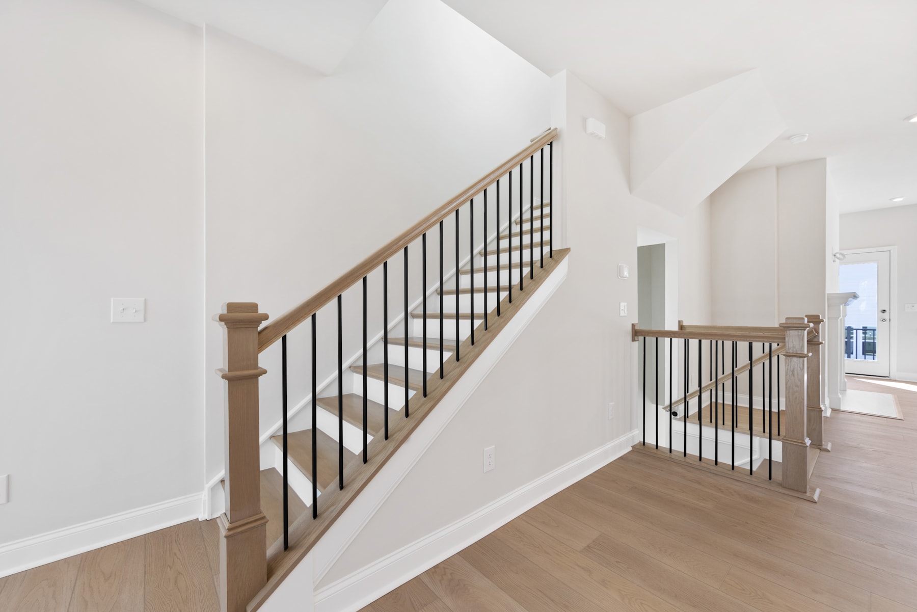 A bright and airy staircase with wooden railings and metal balusters, leading up to a second floor in a modern, minimalist home.