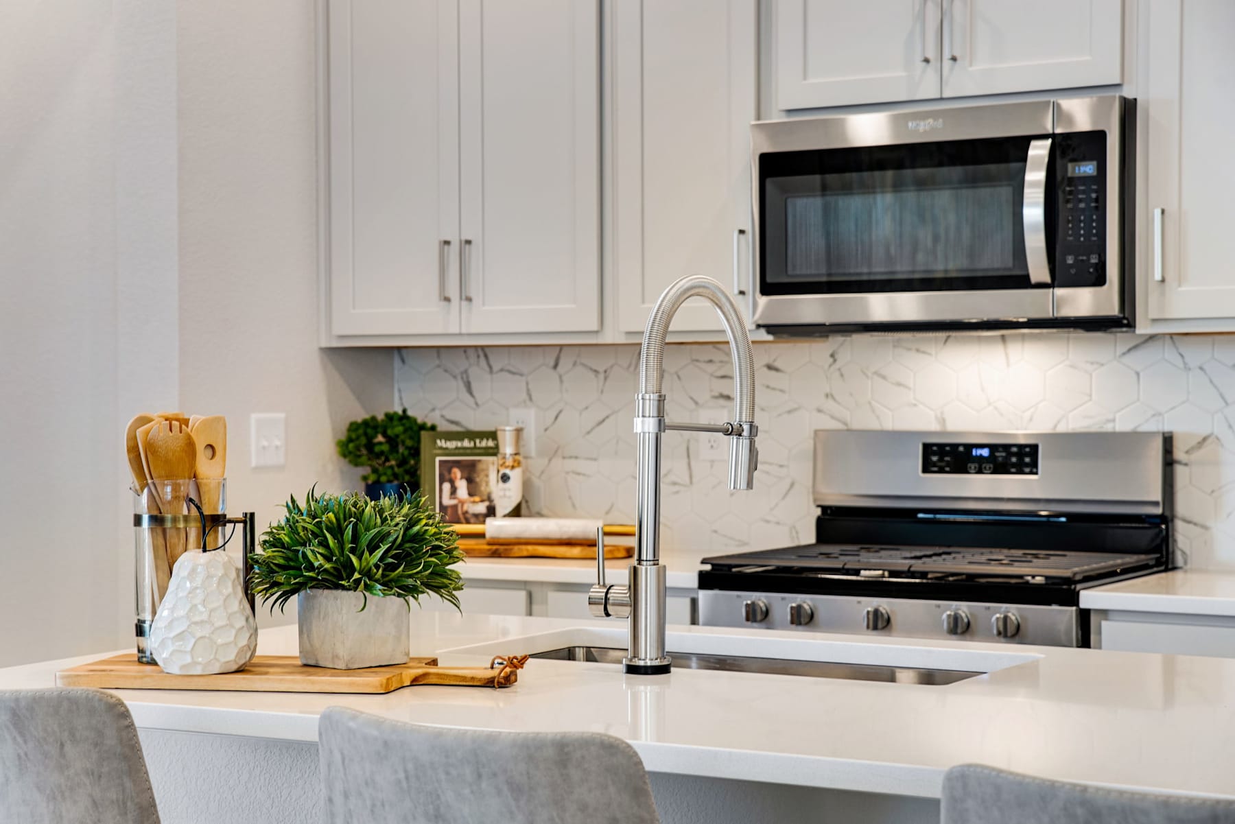 A modern, well-equipped kitchen with white cabinets, stainless steel appliances, and a marble countertop featuring various cooking utensils and decor.