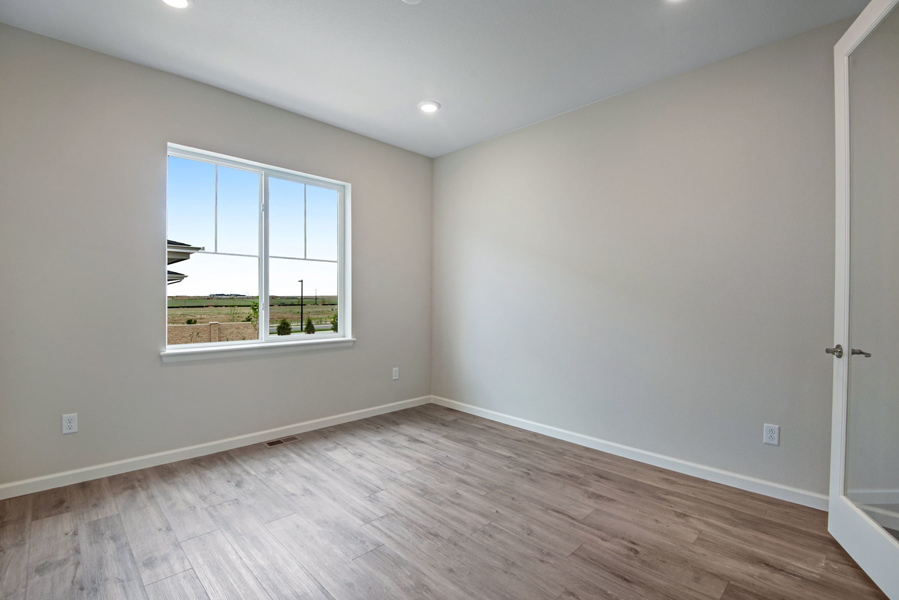 A spacious, well-lit room with a large window overlooking a scenic outdoor landscape, featuring hardwood flooring and neutral-toned walls.