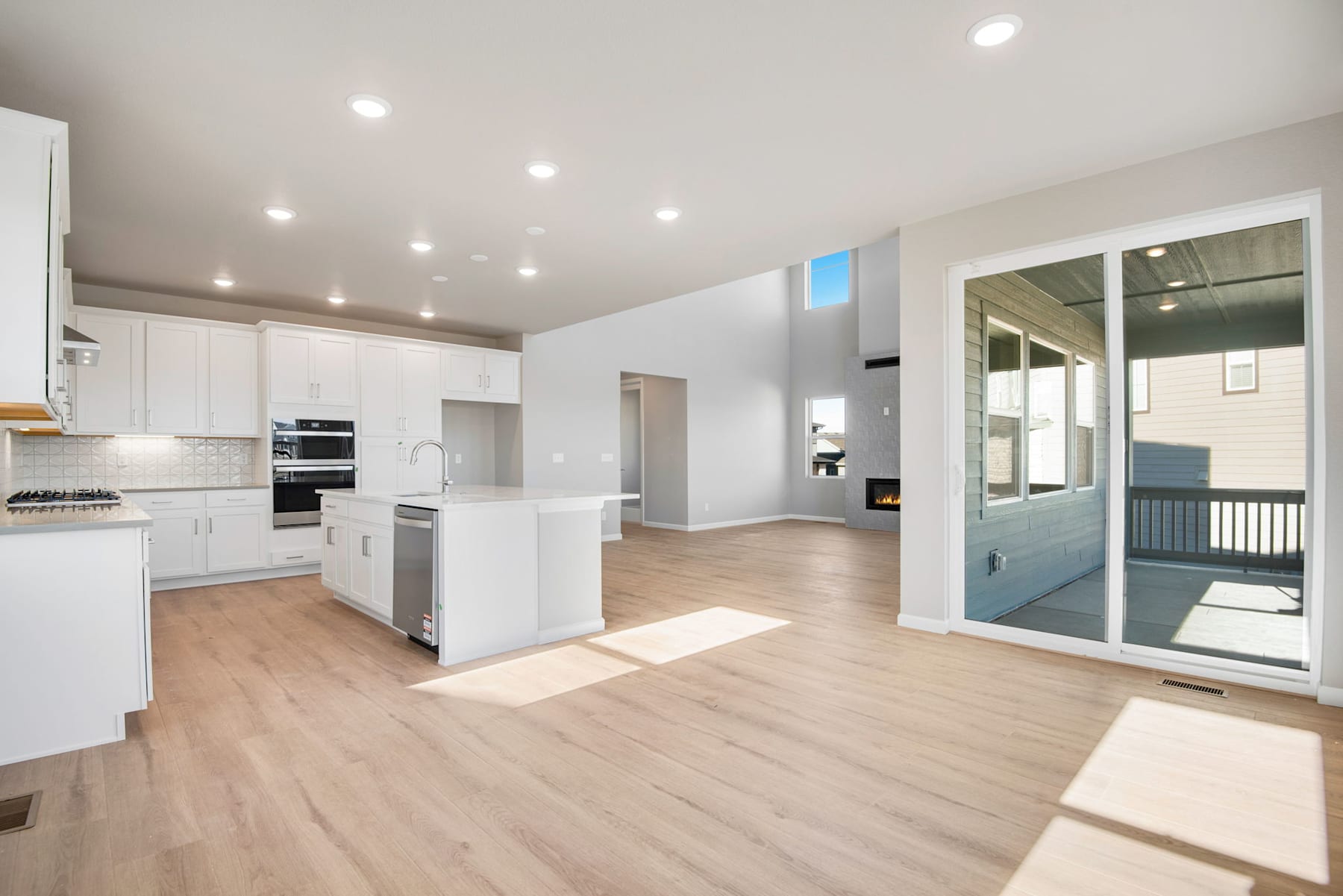 A bright and spacious kitchen with white cabinets, stainless steel appliances, and hardwood floors, leading into an open living area with a sliding glass door to the exterior.