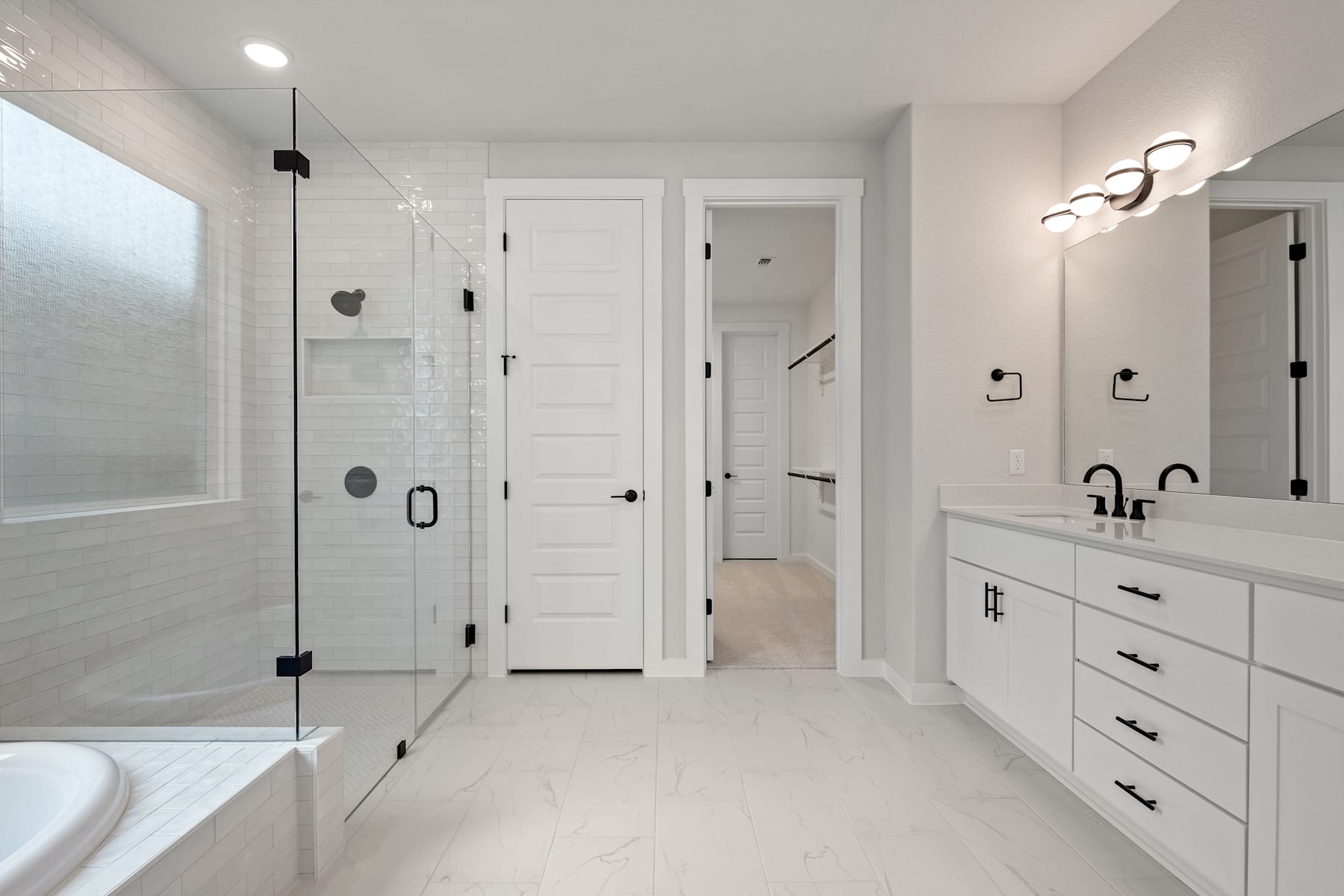A modern, minimalist bathroom with white walls, a glass shower enclosure, and a vanity with drawers.