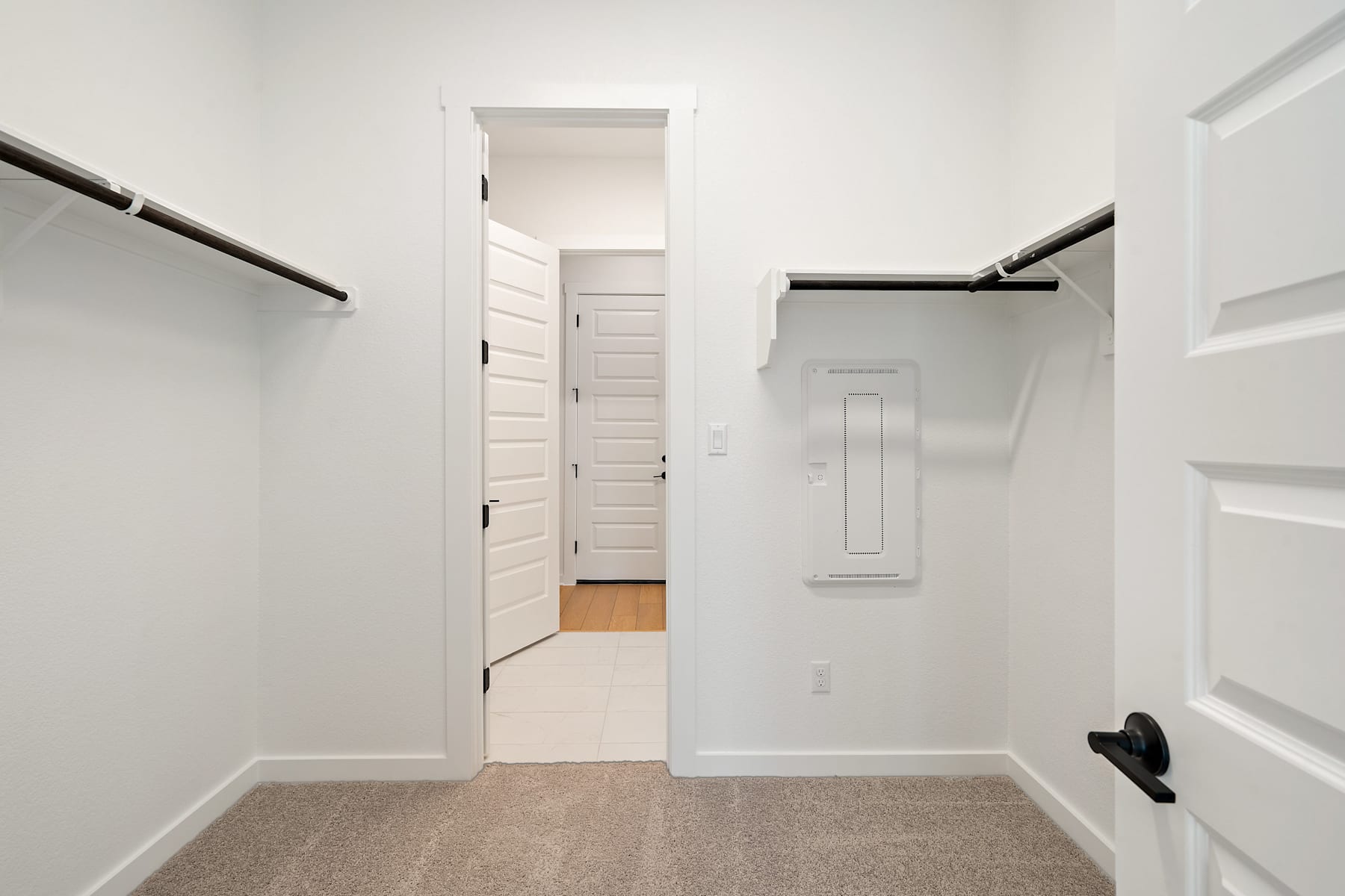 A bright, minimalist hallway with white walls, a wooden door, and a closet or storage space visible in the background.