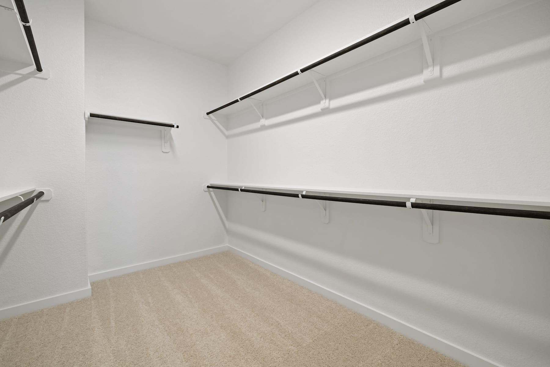 A spacious, well-lit closet with white walls, wooden shelves, and a beige carpeted floor.