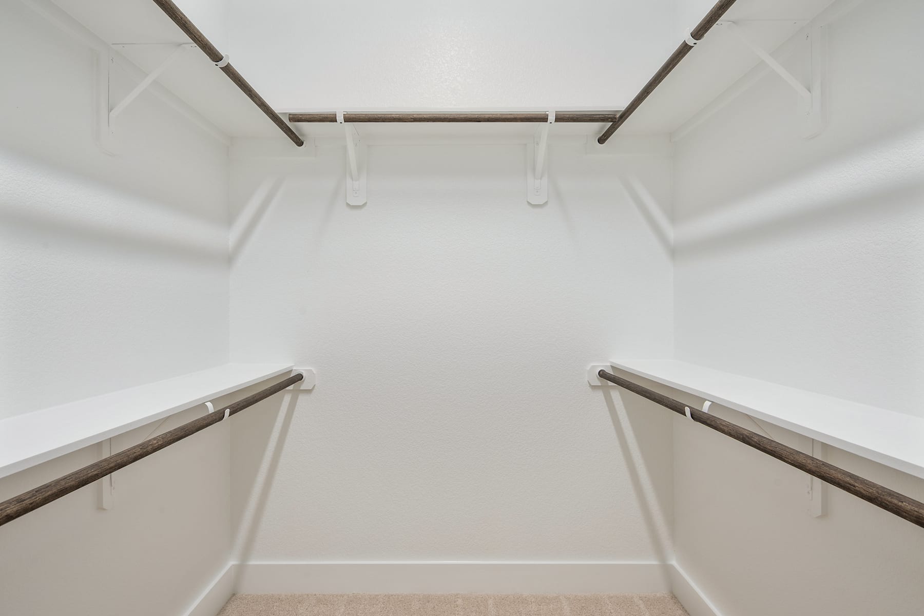 A minimalist, well-lit closet space with white walls, wooden shelves, and metal rods for hanging clothes.