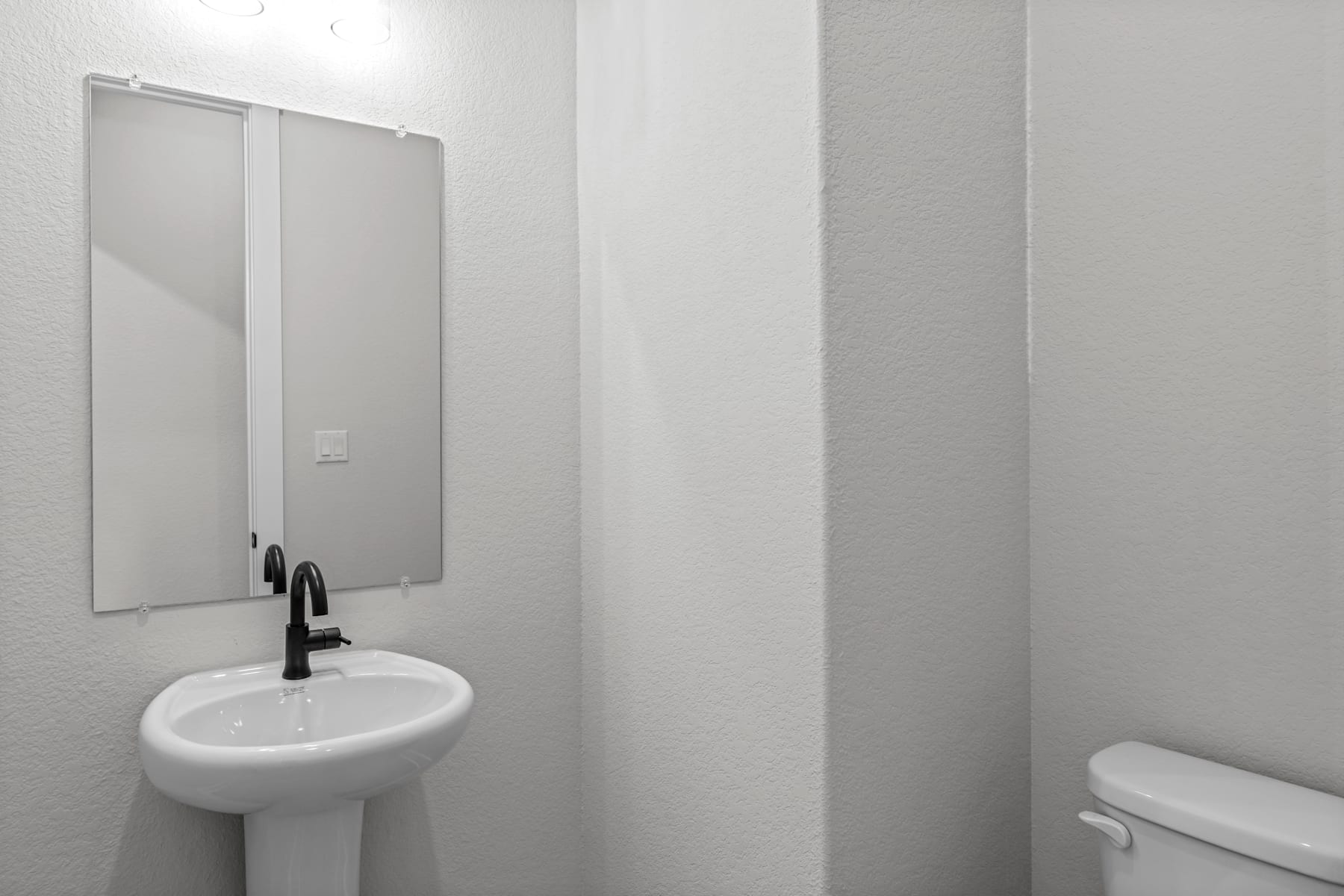 A minimalist bathroom with a white sink, mirror, and toilet against a plain white wall.