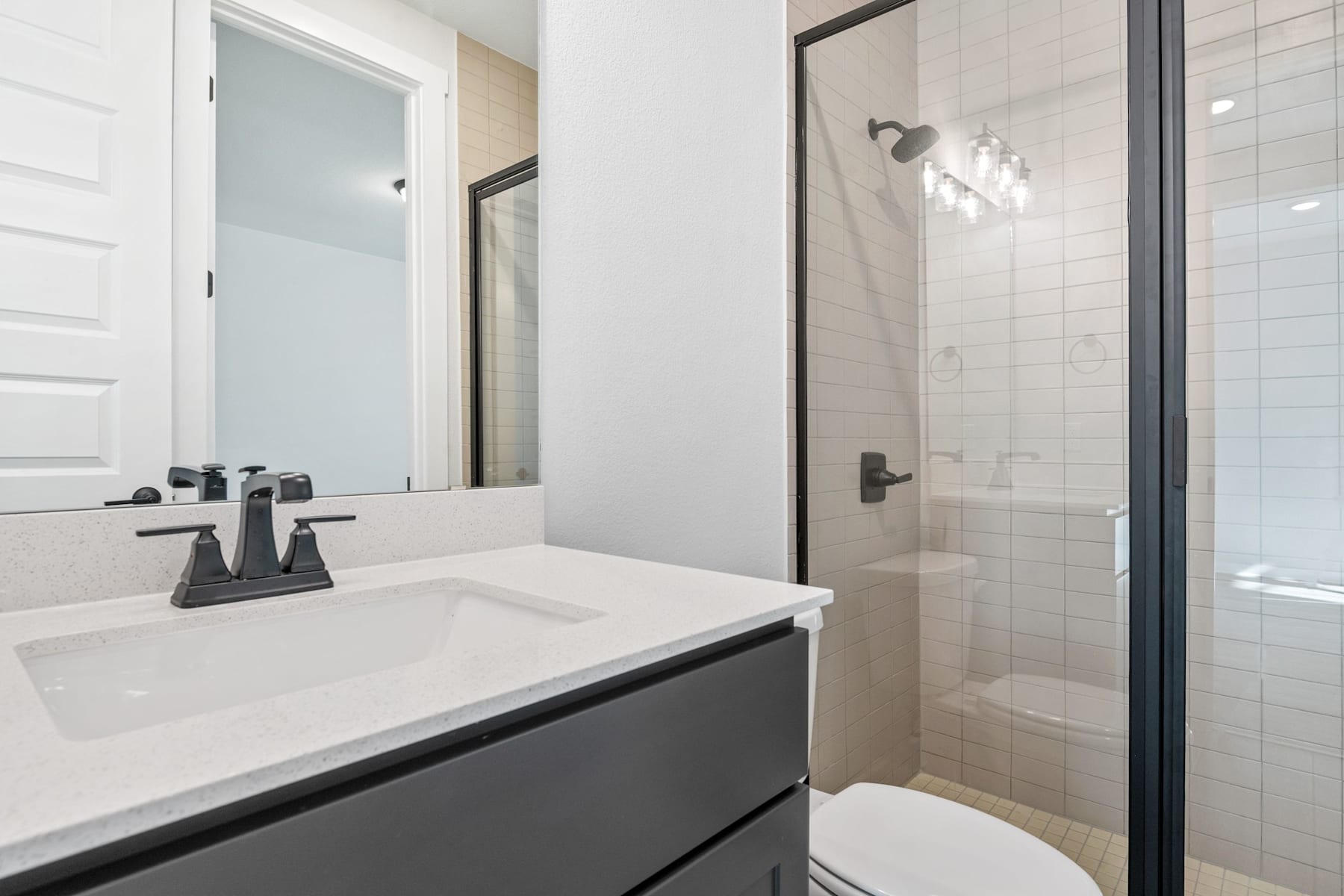 A modern bathroom with a white vanity, black faucet, and a glass-enclosed shower in the background.