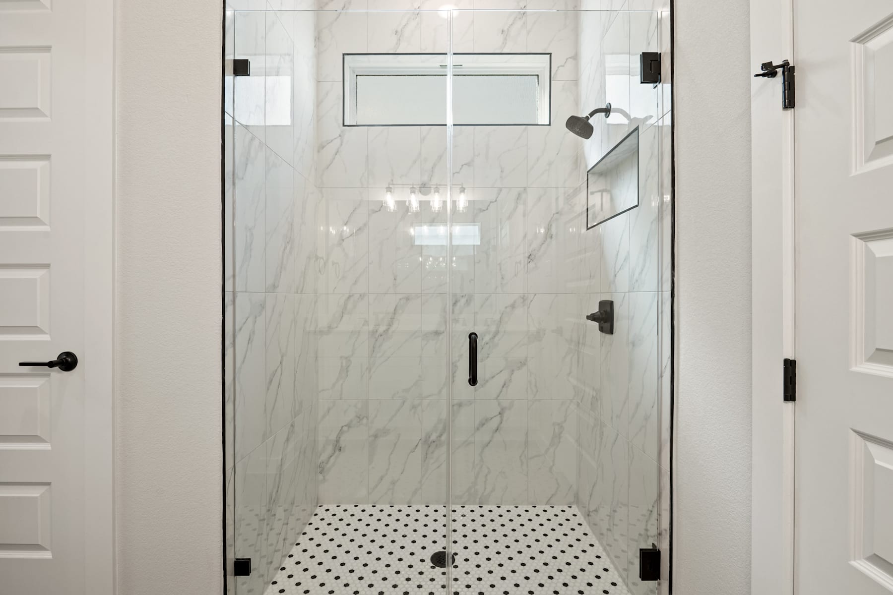 A modern, minimalist bathroom with a glass shower enclosure, white marble walls, and a black and white tiled floor.