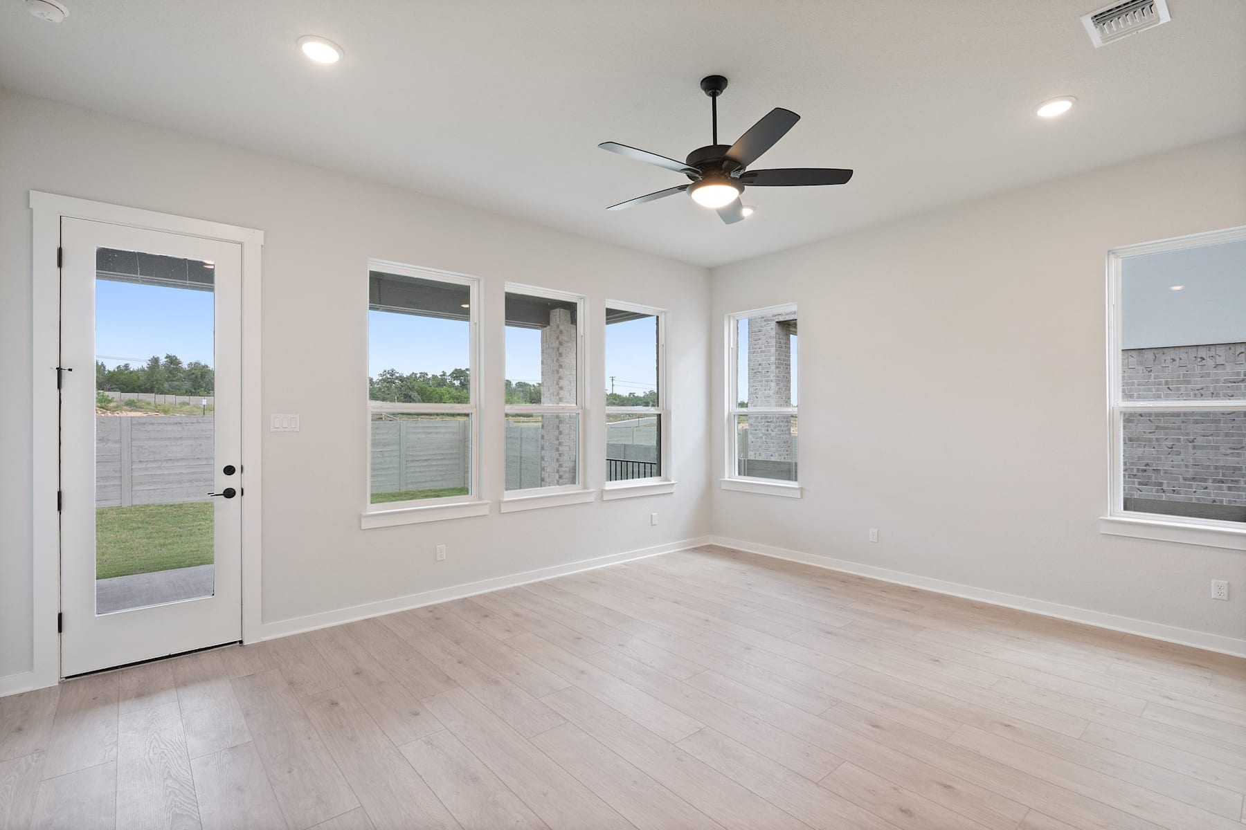 A bright and airy room with a ceiling fan, hardwood floors, and large windows overlooking a grassy outdoor area.