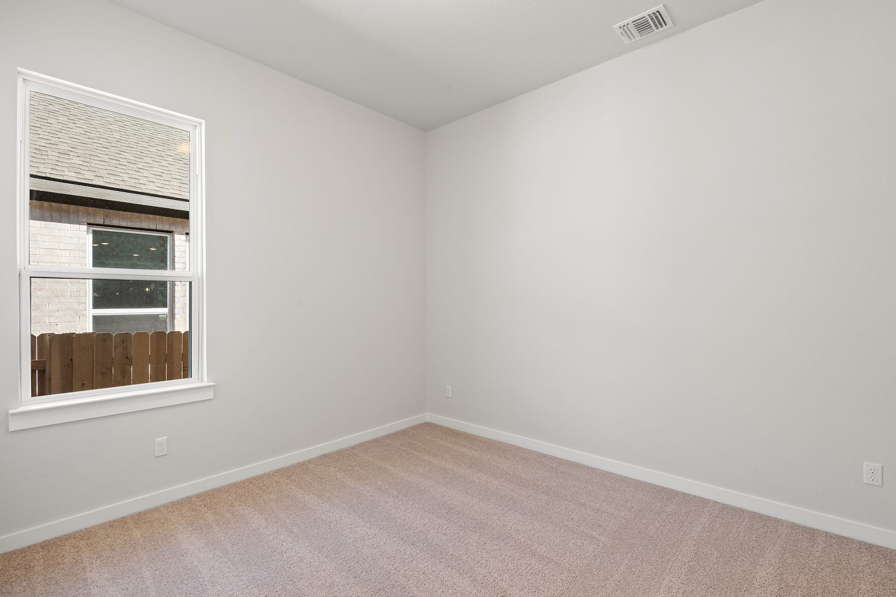 A sparsely furnished room with a window, white walls, and a light-colored hardwood floor.