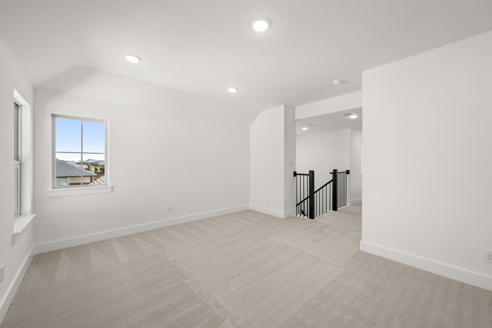 A bright, open-concept room with white walls, a window, and a hardwood floor leading to a staircase with a black railing.