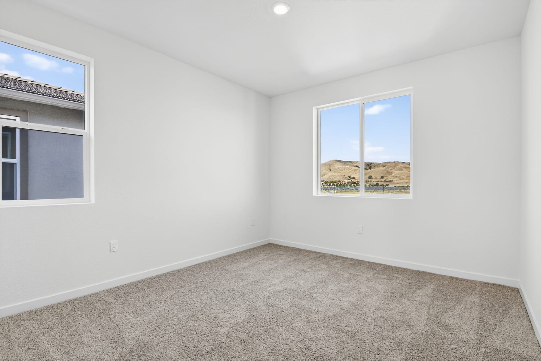 A bright, empty room with large windows overlooking a desert landscape in the background.