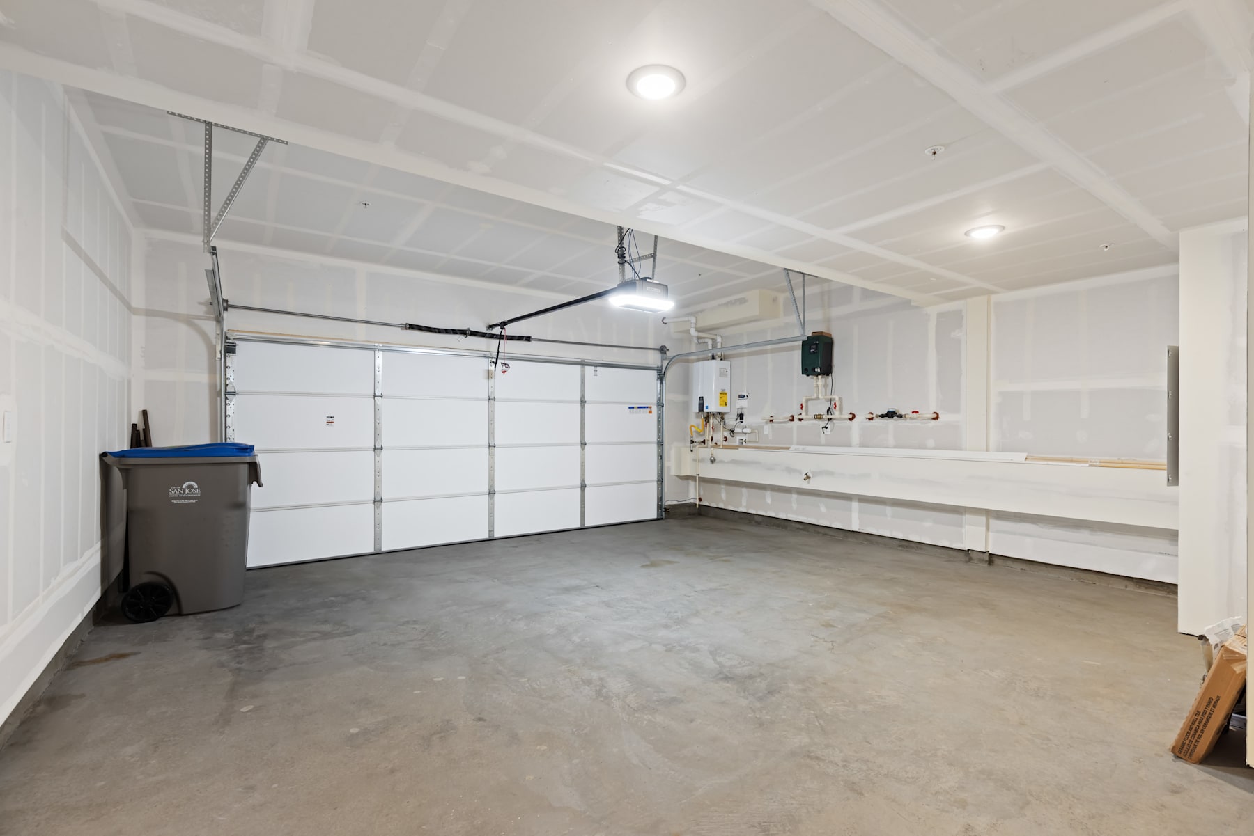 A spacious, well-lit garage interior with a concrete floor, white walls, and various storage and utility items visible.