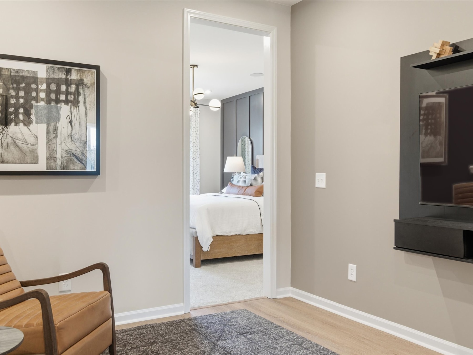 A cozy bedroom with a wooden chair in the foreground and a partially visible bed in the background, framed by a white doorway.