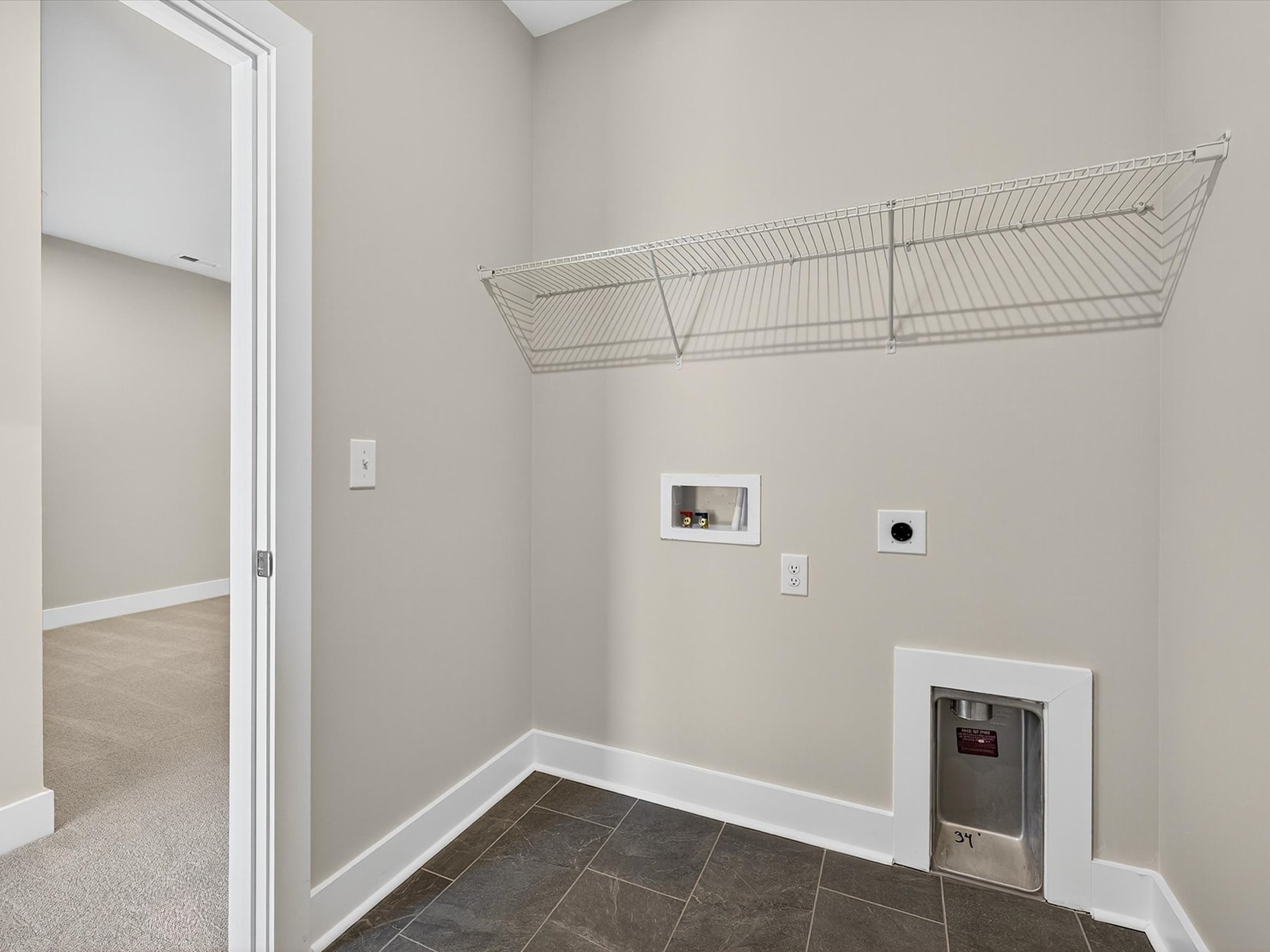 A spacious entryway with a wire storage rack mounted on the wall, a tile floor, and a doorway leading to another room.