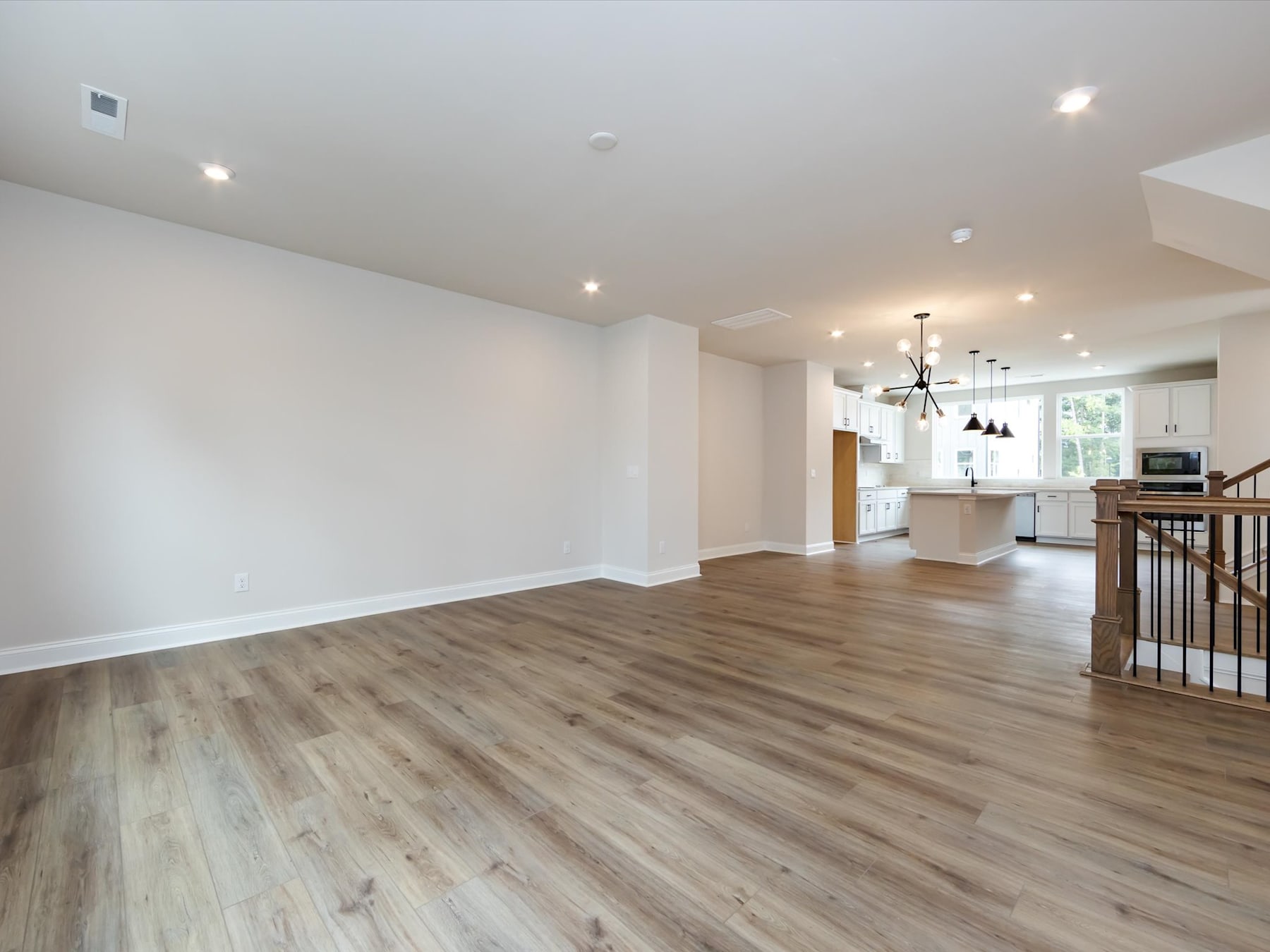A spacious, open-concept living area with hardwood floors, recessed lighting, and a kitchen visible in the background.