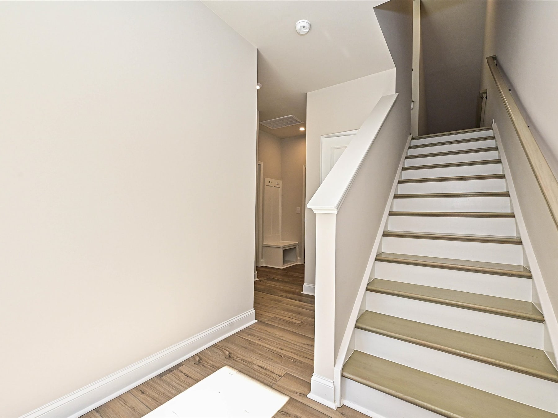 A staircase with wooden steps leading up to a hallway, with a white wall and a doorway visible in the background.