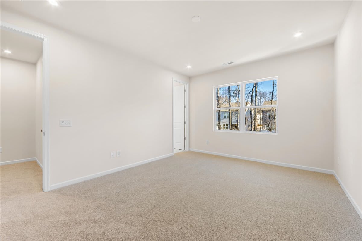 A bright, spacious room with white walls, a large window, and a carpeted floor.