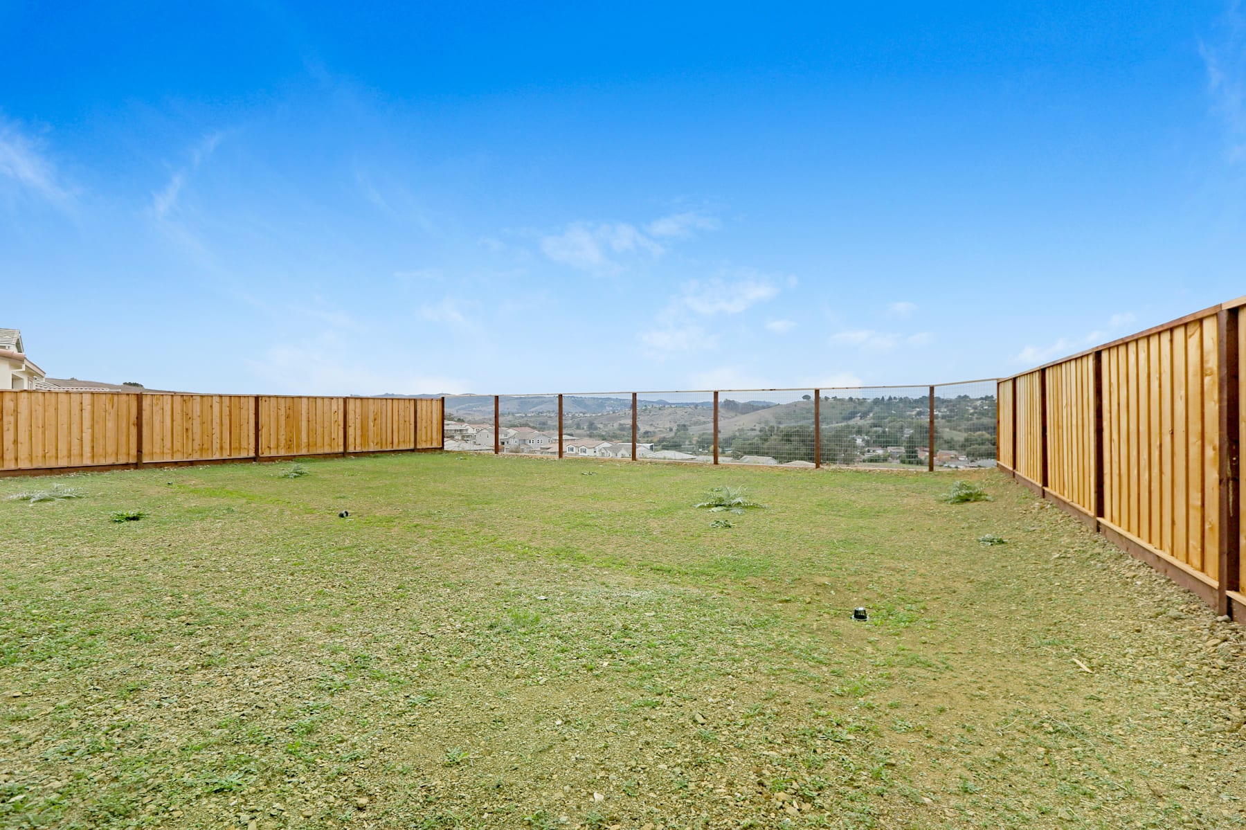 A grassy backyard with a wooden fence surrounding it, overlooking a scenic landscape in the distance under a clear blue sky.