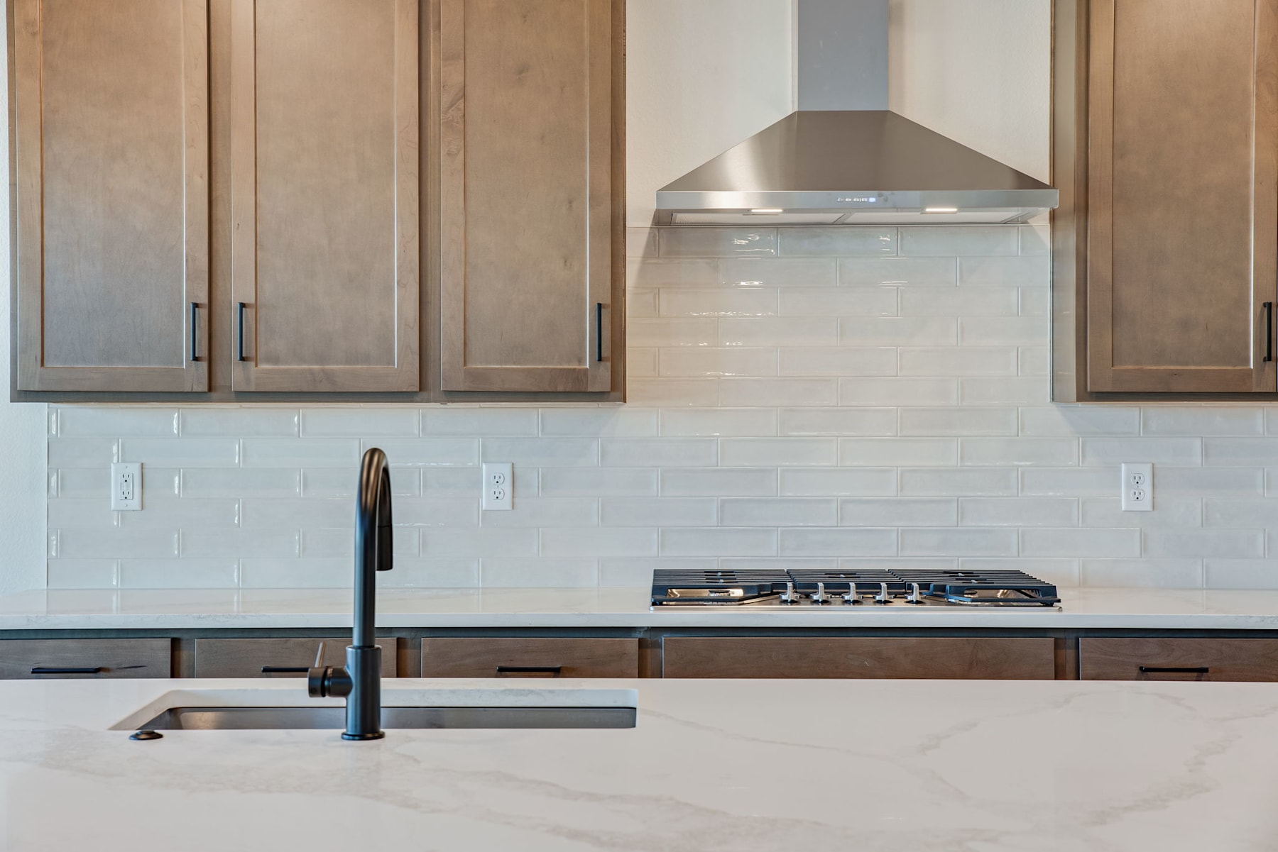 A modern kitchen with wooden cabinets, a stainless steel range hood, and a marble countertop with a sink and gas stove.
