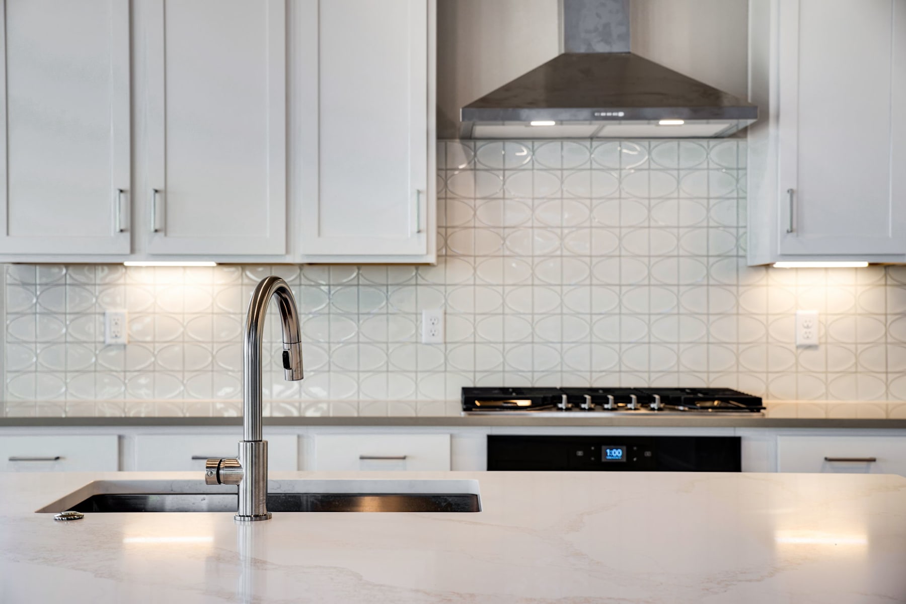 A modern kitchen with white cabinets, a stainless steel sink, and a gas stove with a range hood above it.