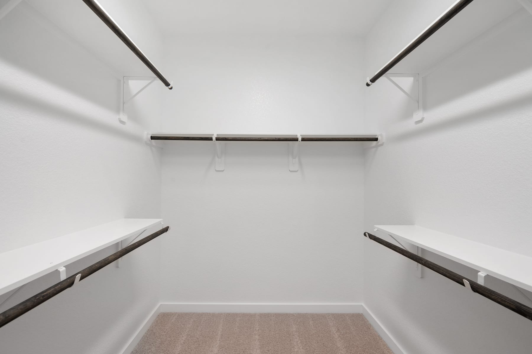 A minimalist, well-lit closet space with white walls, wooden shelves, and metal hanging rods.