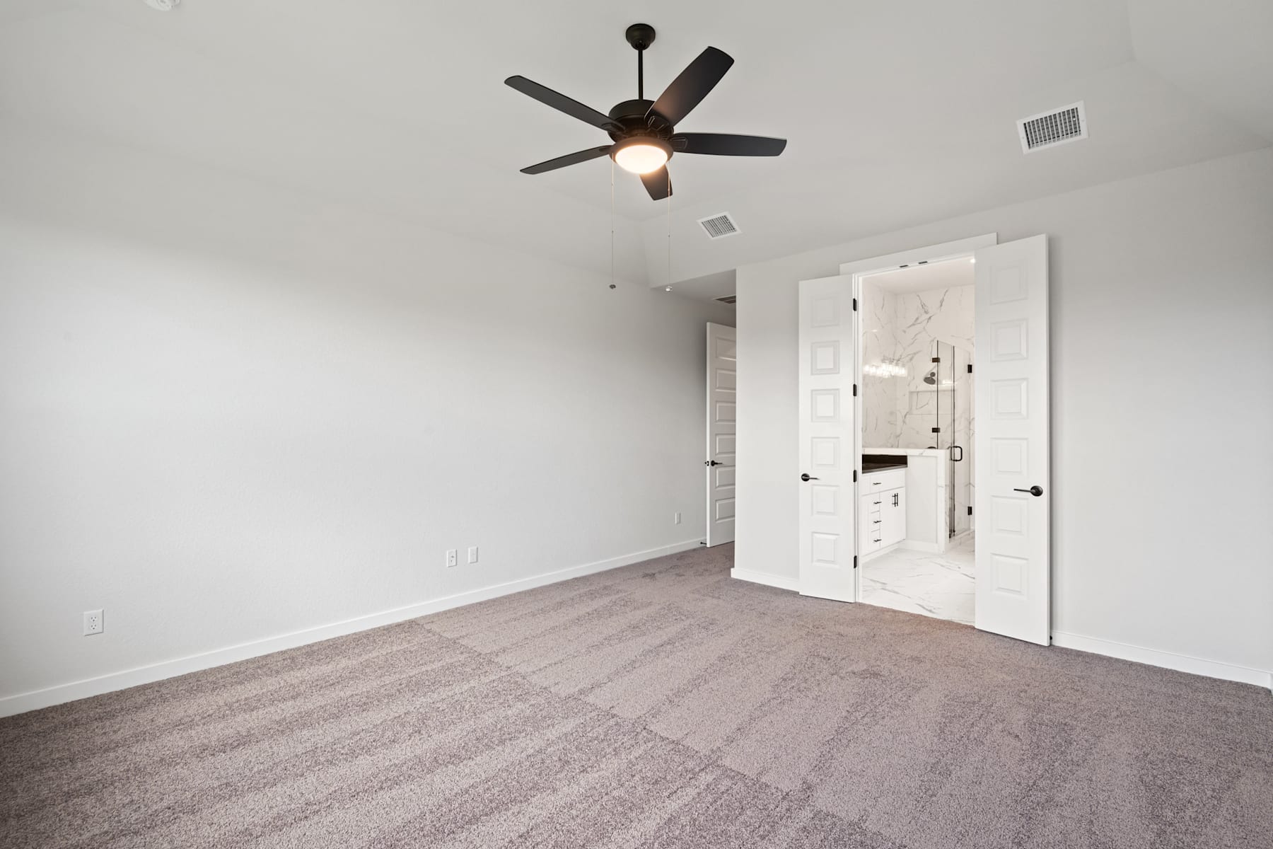 A spacious, minimalist bedroom with a ceiling fan and white walls, featuring a carpeted floor and a pair of white doors in the background.