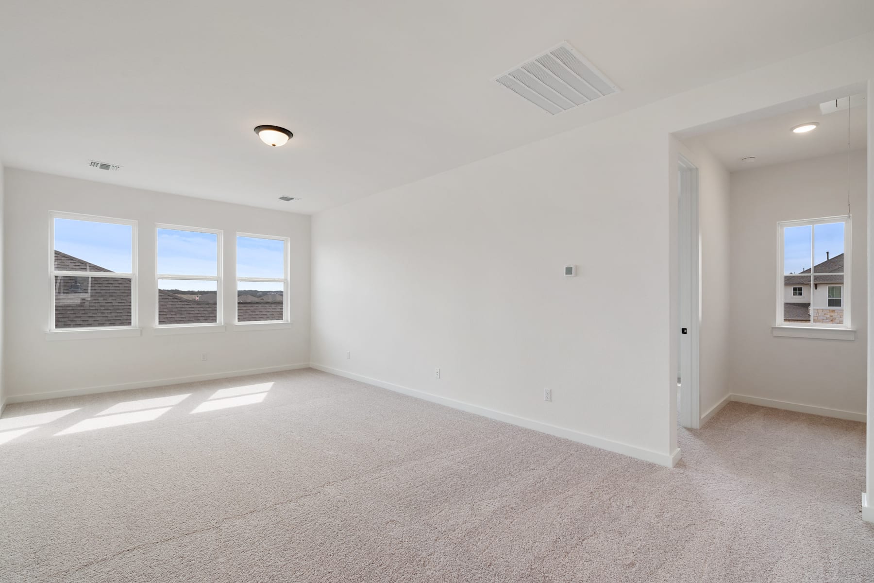 An empty, bright, and spacious room with white walls, a carpeted floor, and several windows allowing natural light to fill the space.