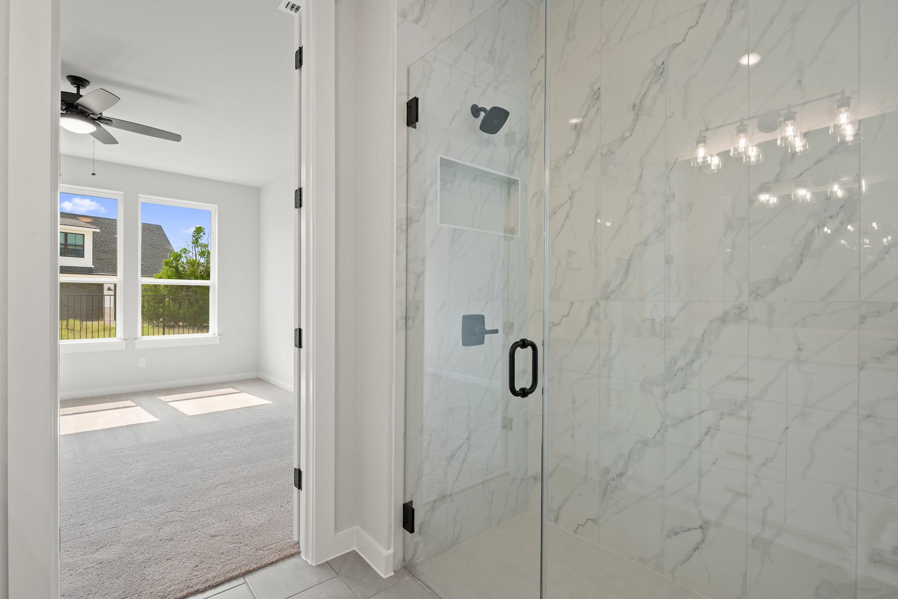 A bright and spacious bathroom with a marble-tiled wall, a glass shower door, and a window overlooking the outdoor scenery.