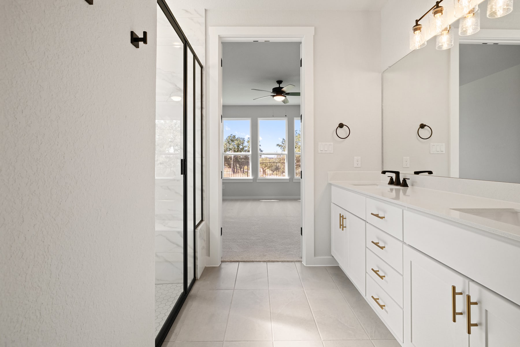 A bright and spacious bathroom with white walls, a vanity with drawers, and a window overlooking an outdoor scene.