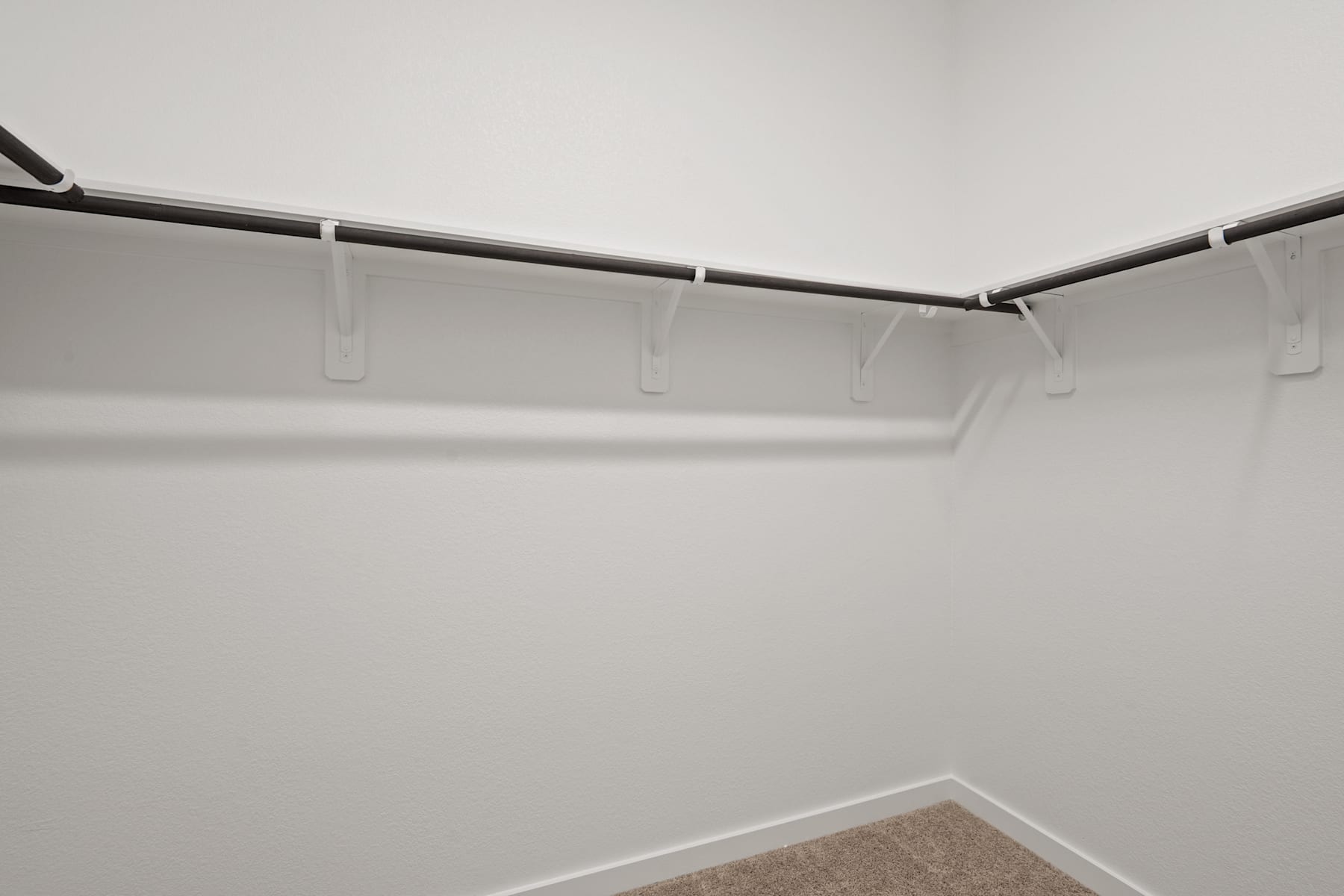 A white wall with a metal clothing rod and hangers in the foreground, creating a minimalist and organized storage space.