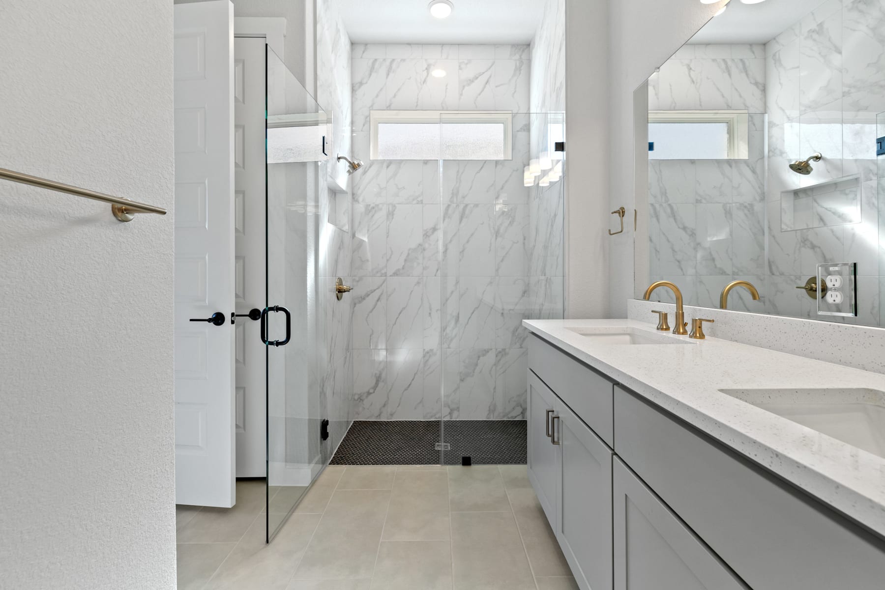 A modern, minimalist bathroom with a gray vanity, white marble walls, and a glass shower enclosure.