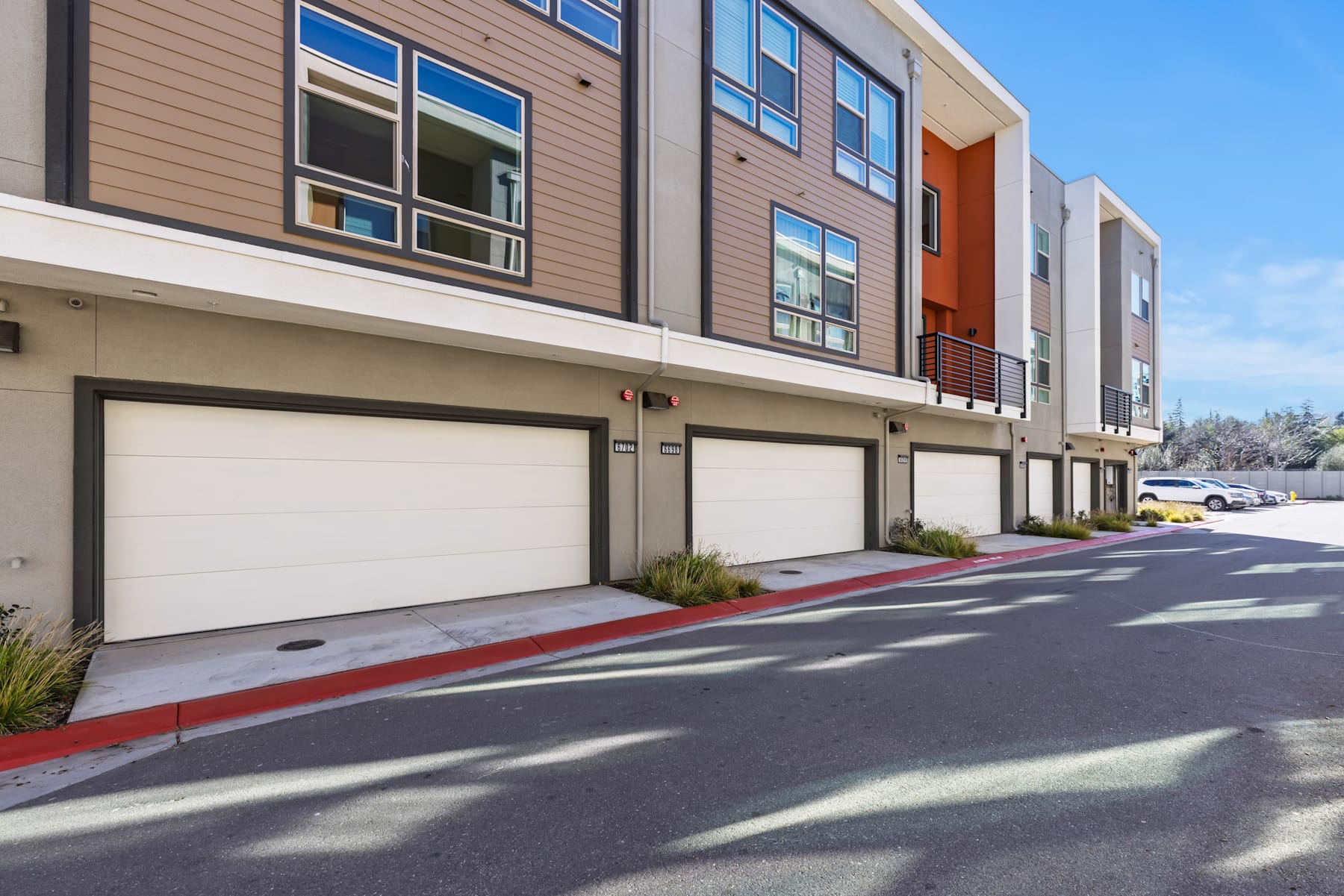 The image shows a modern multi-story residential building with garages in the foreground and a clear blue sky in the background.