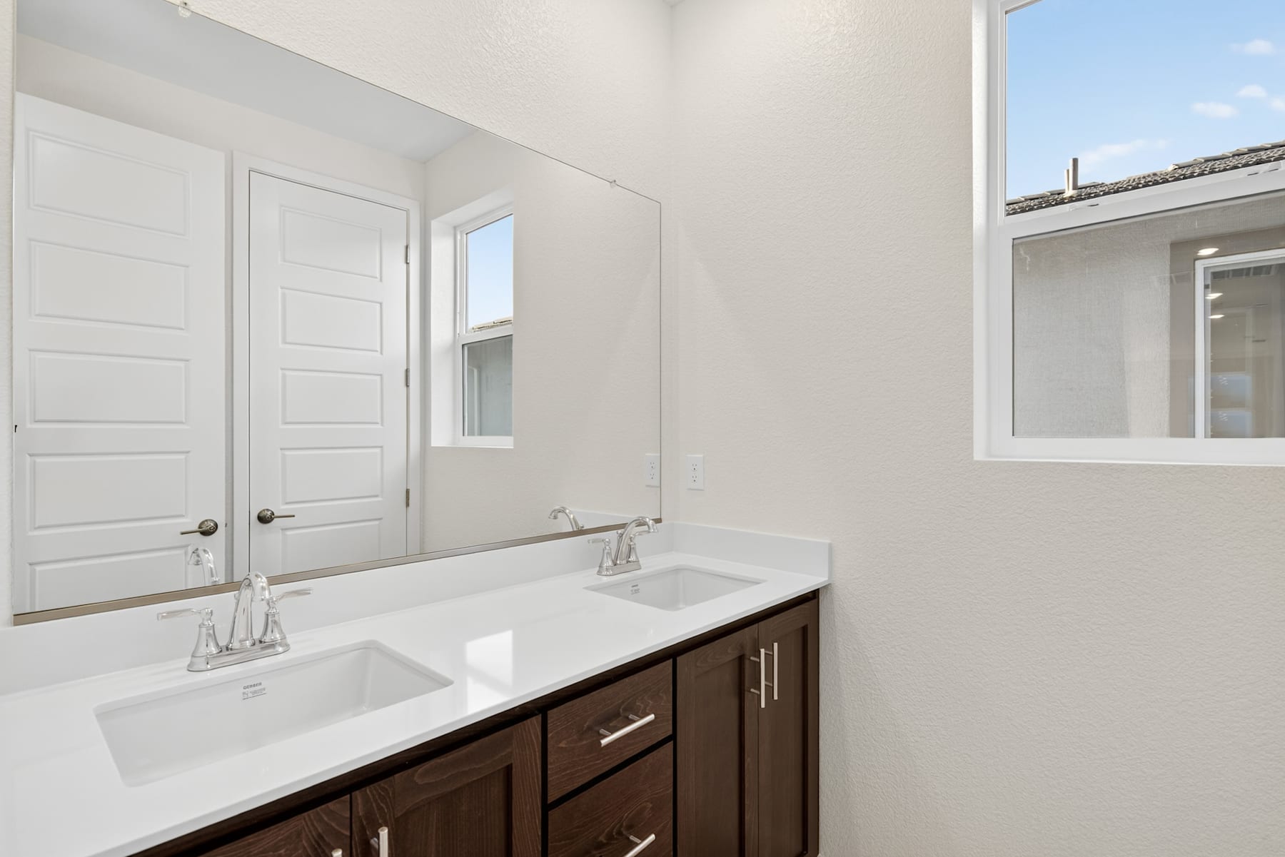 A modern bathroom with a white vanity, double sinks, and a large window providing natural light.