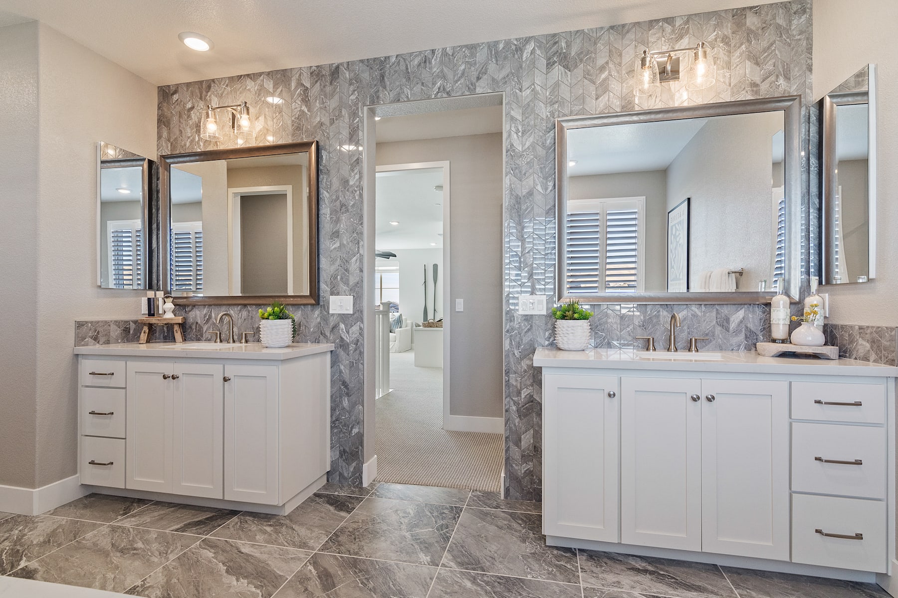A modern and well-designed bathroom with white cabinets, marble-patterned walls, and a tiled floor. The room features multiple mirrors and lighting fixtures, creating a bright and spacious atmosphere.