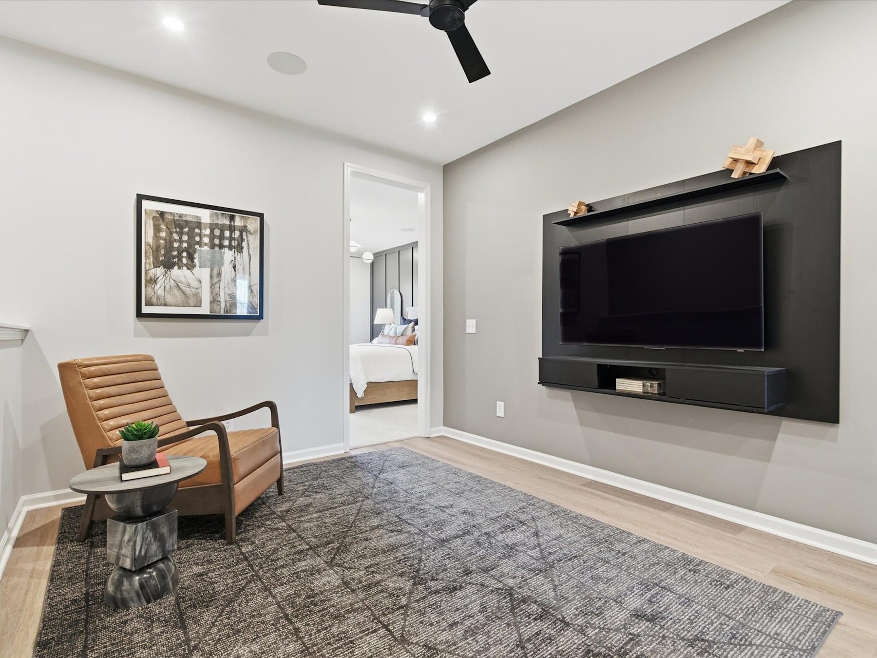 A modern and minimalist living room with a large TV mounted on the wall, a comfortable armchair, and a patterned rug on the hardwood floor.