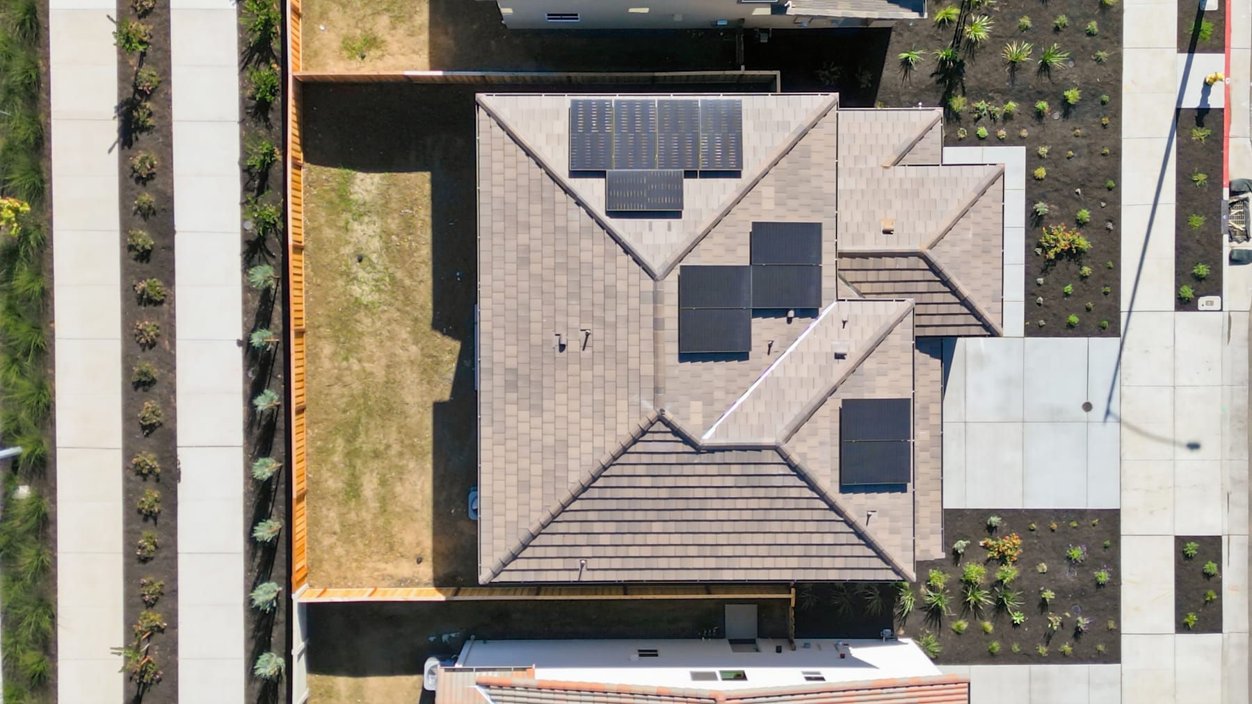 The image shows a modern, angular building with a complex roofline and various architectural elements, surrounded by lush greenery in the background.