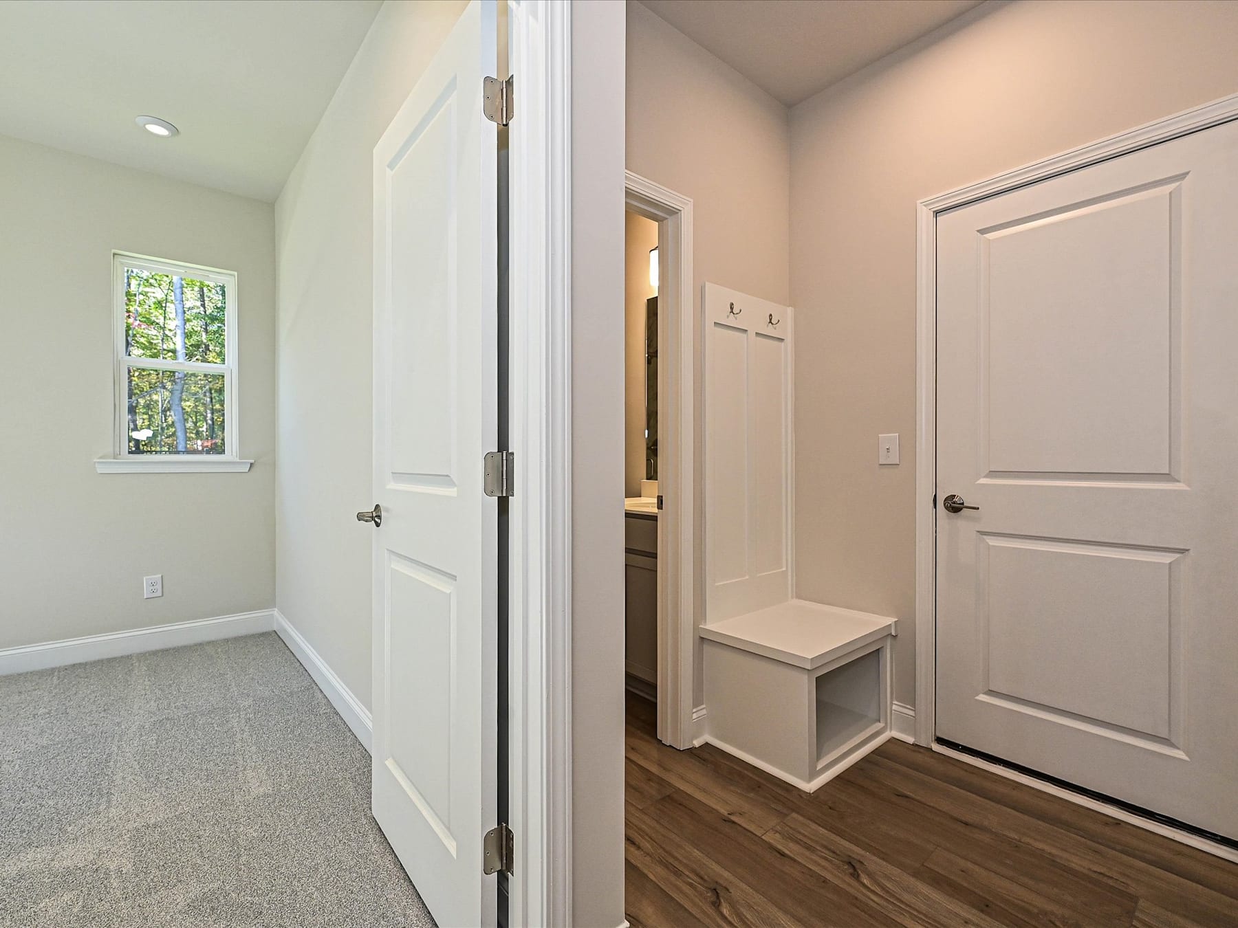 A bright and airy hallway with white walls, wooden floors, and a small bench next to a closed door, leading to another room.