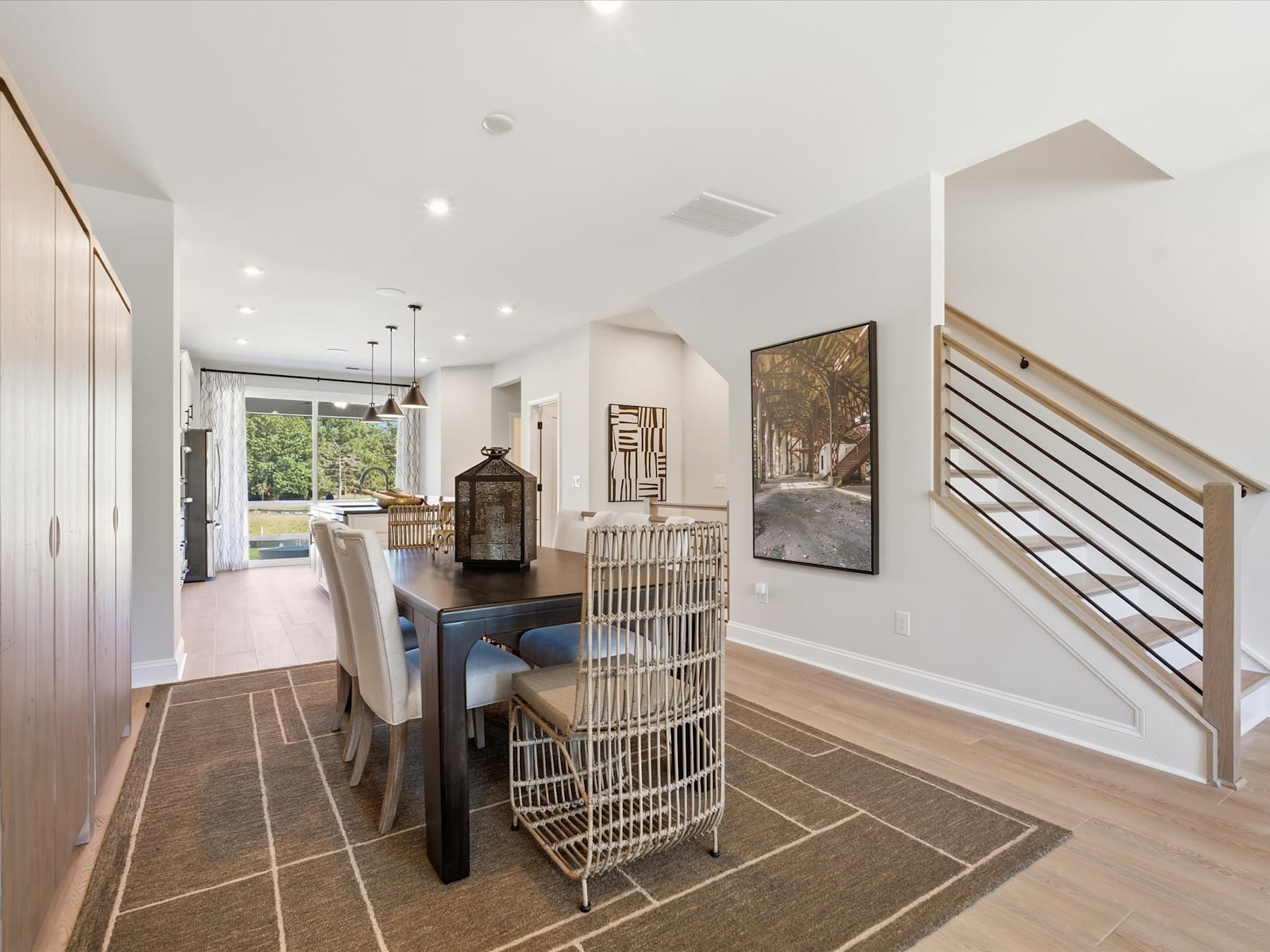 A modern and spacious open-plan living area with a dining table, chairs, and decorative elements, surrounded by large windows and a staircase leading to an upper level.